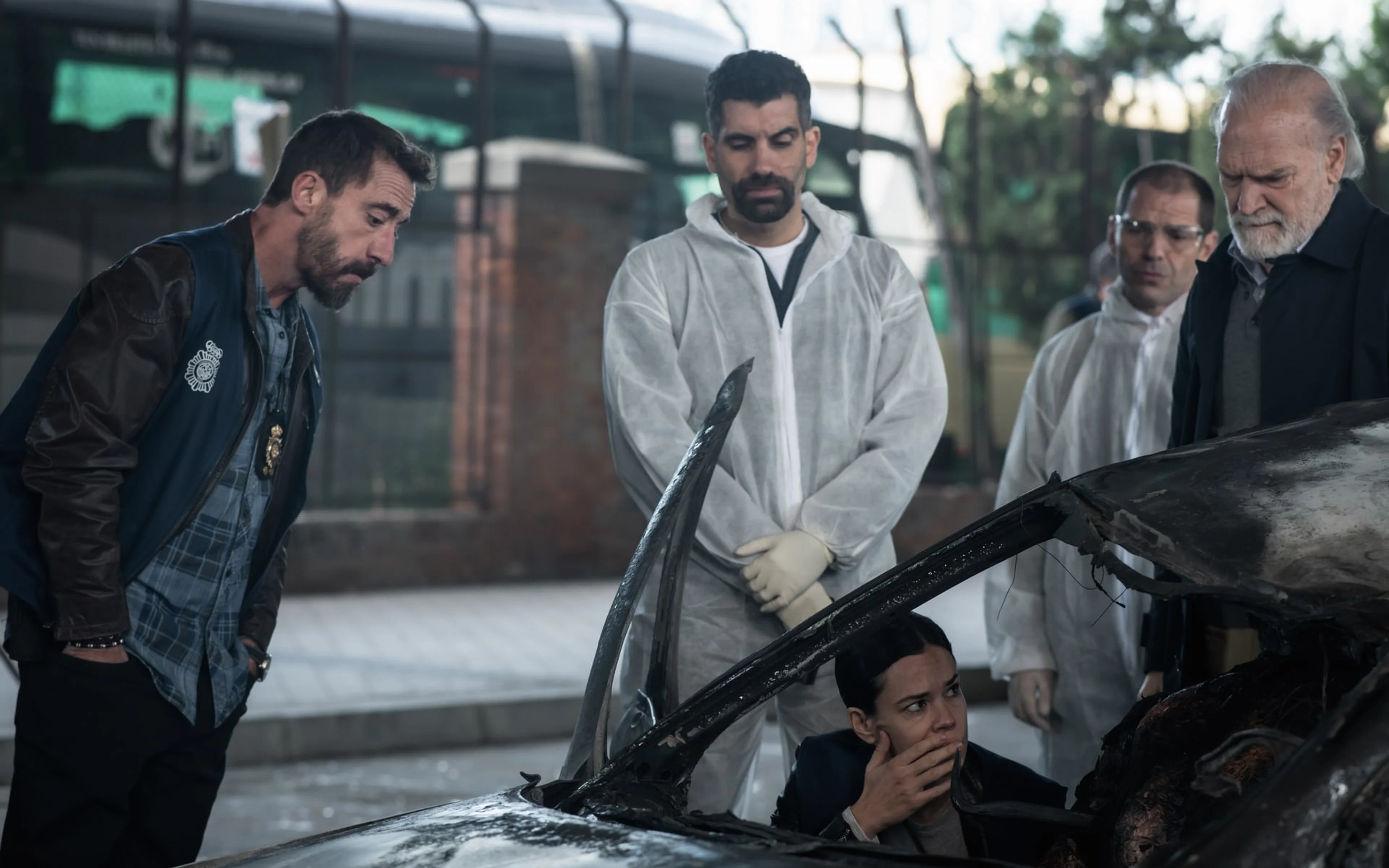 Several people examine a badly damaged car in an official still from Collision Course.