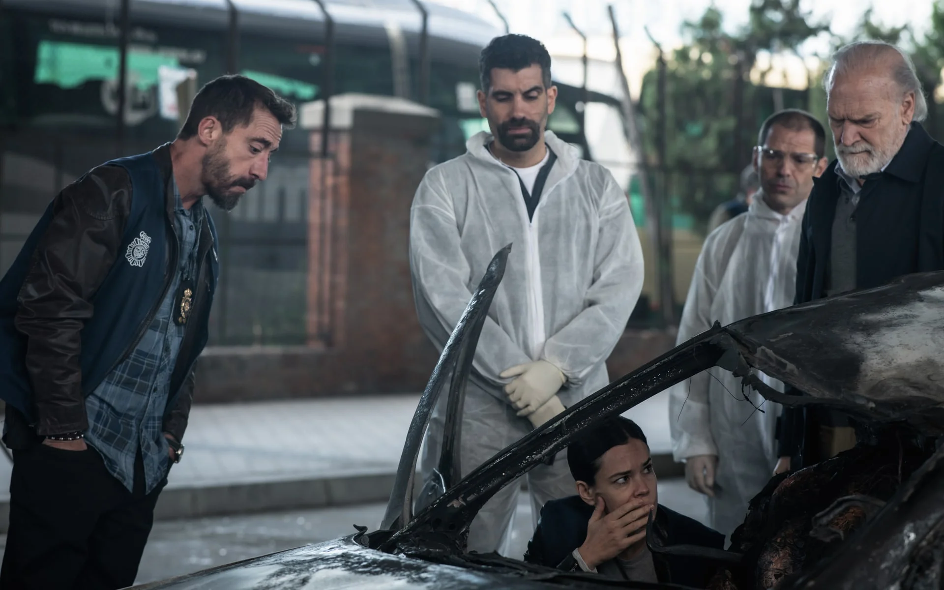Several people examine a badly damaged car in an official still from Collision Course.