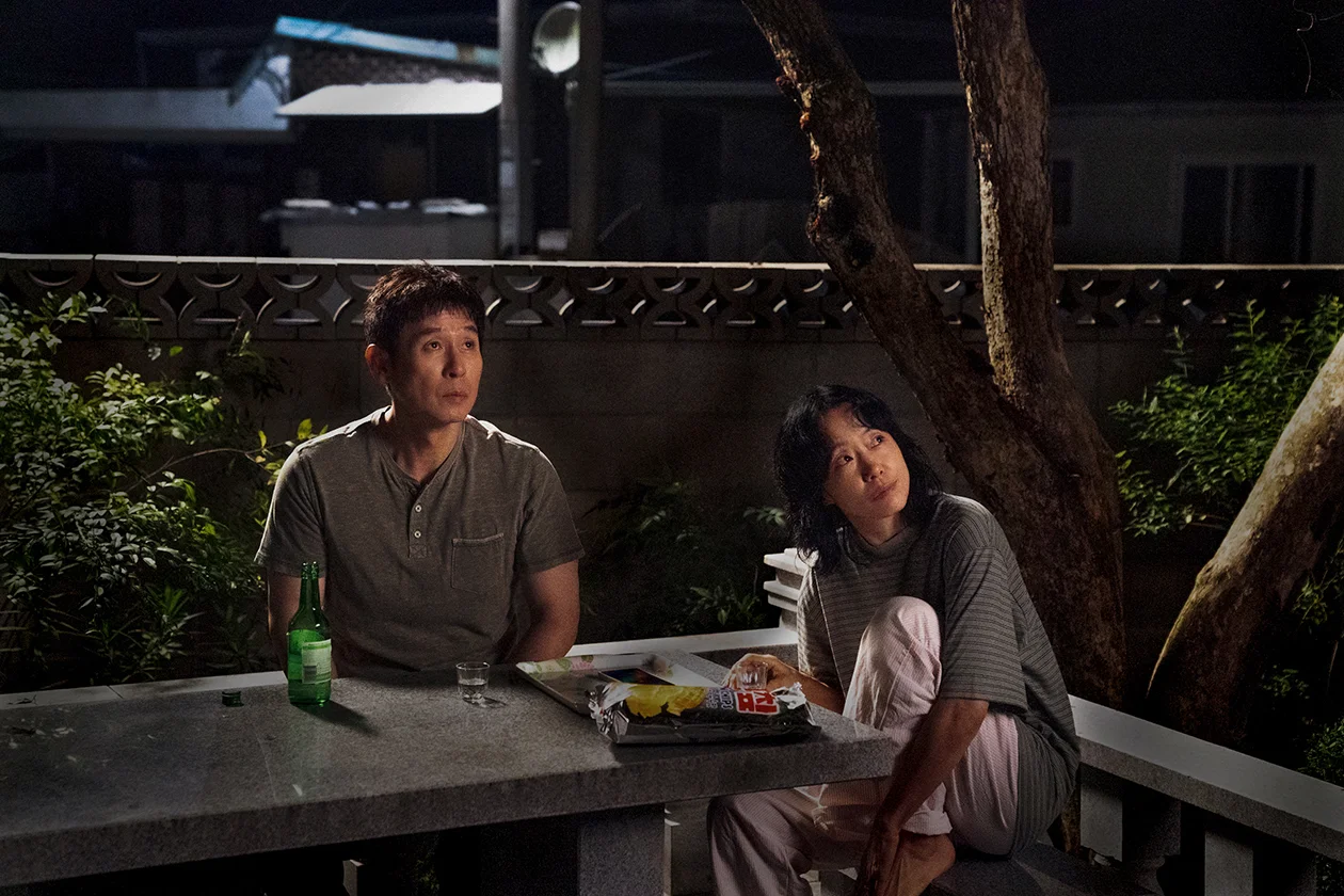 Ho-seok and Mi-ok sit at an outdoor table at night.
