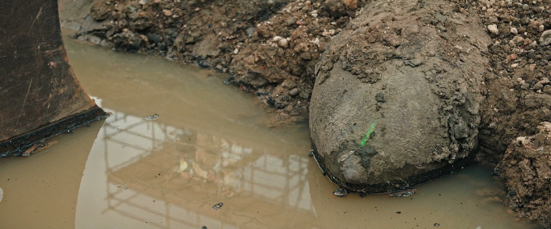 An unexploded bomb lies in muddy water beside an excavator at a London building site.
