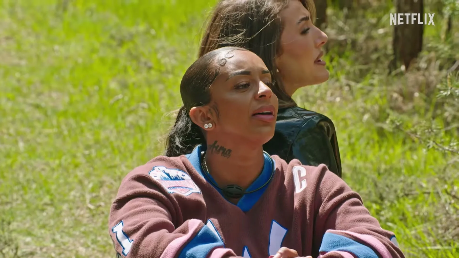 Two Outside contestants react while sitting outdoors in the official Netflix trailer.