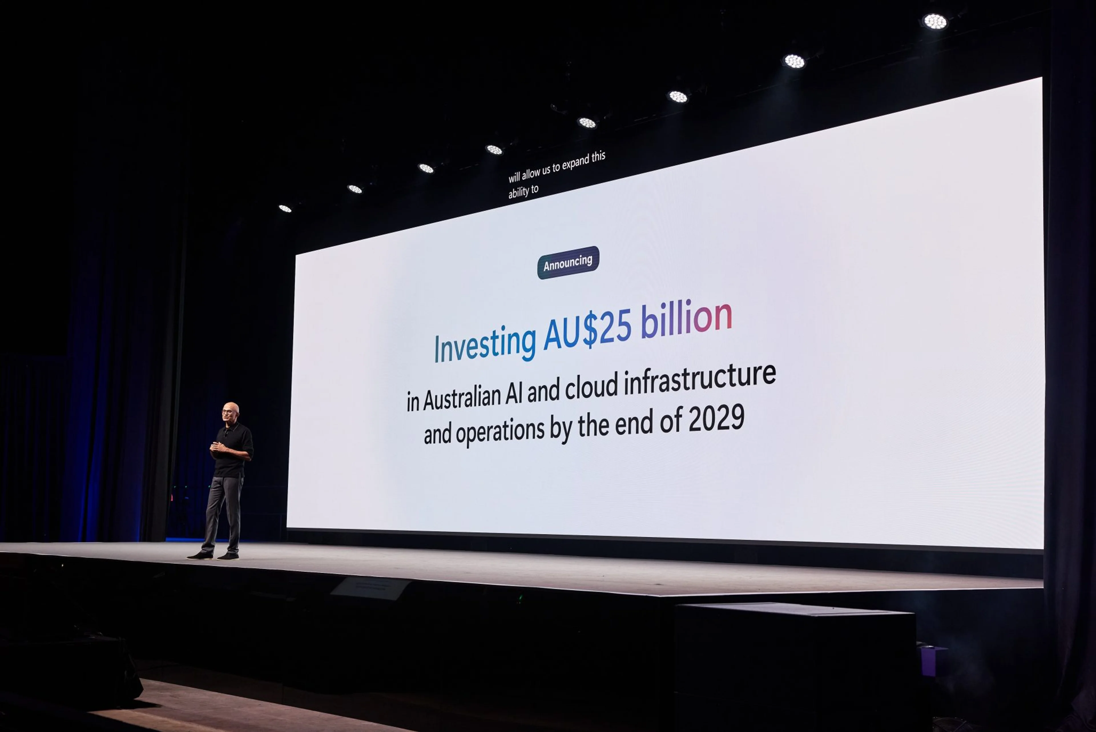Satya Nadella stands on a blue-lit stage during a Microsoft keynote.