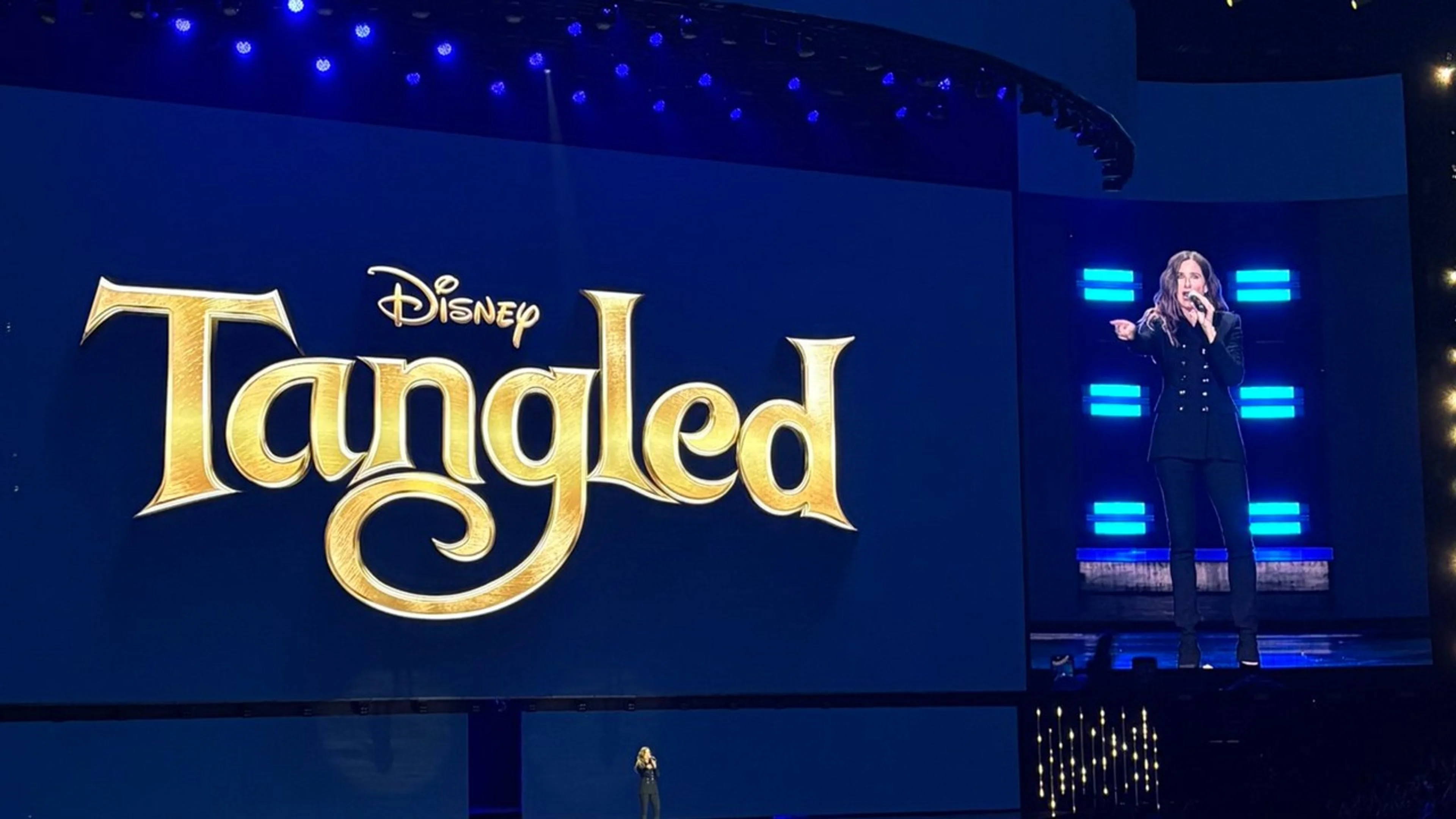 The Disney Tangled logo and Kathryn Hahn speaking during the live-action movie presentation at D23 2026.