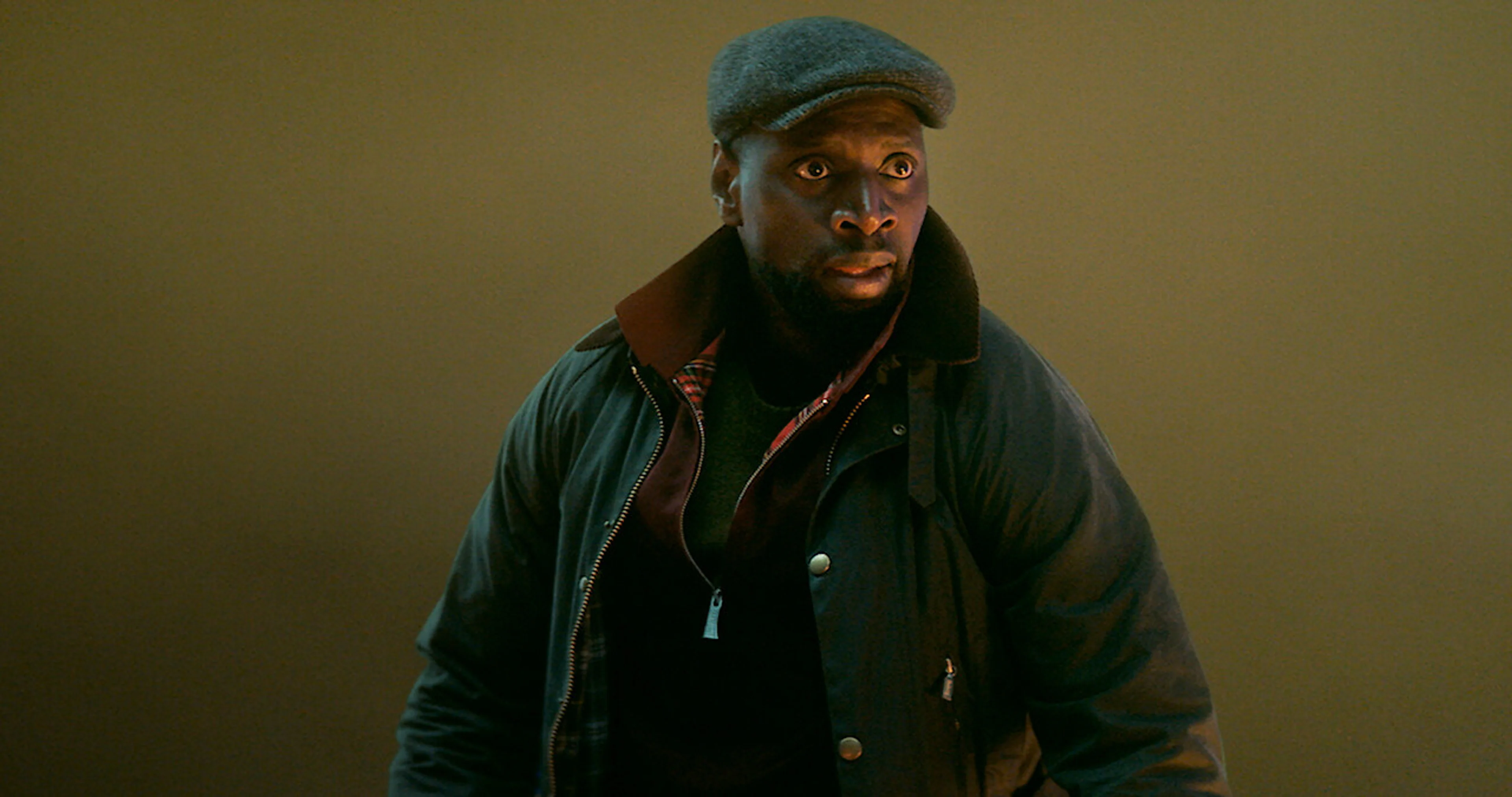 Omar Sy stands on a rooftop in Paris while wearing a disguise in Lupin.
