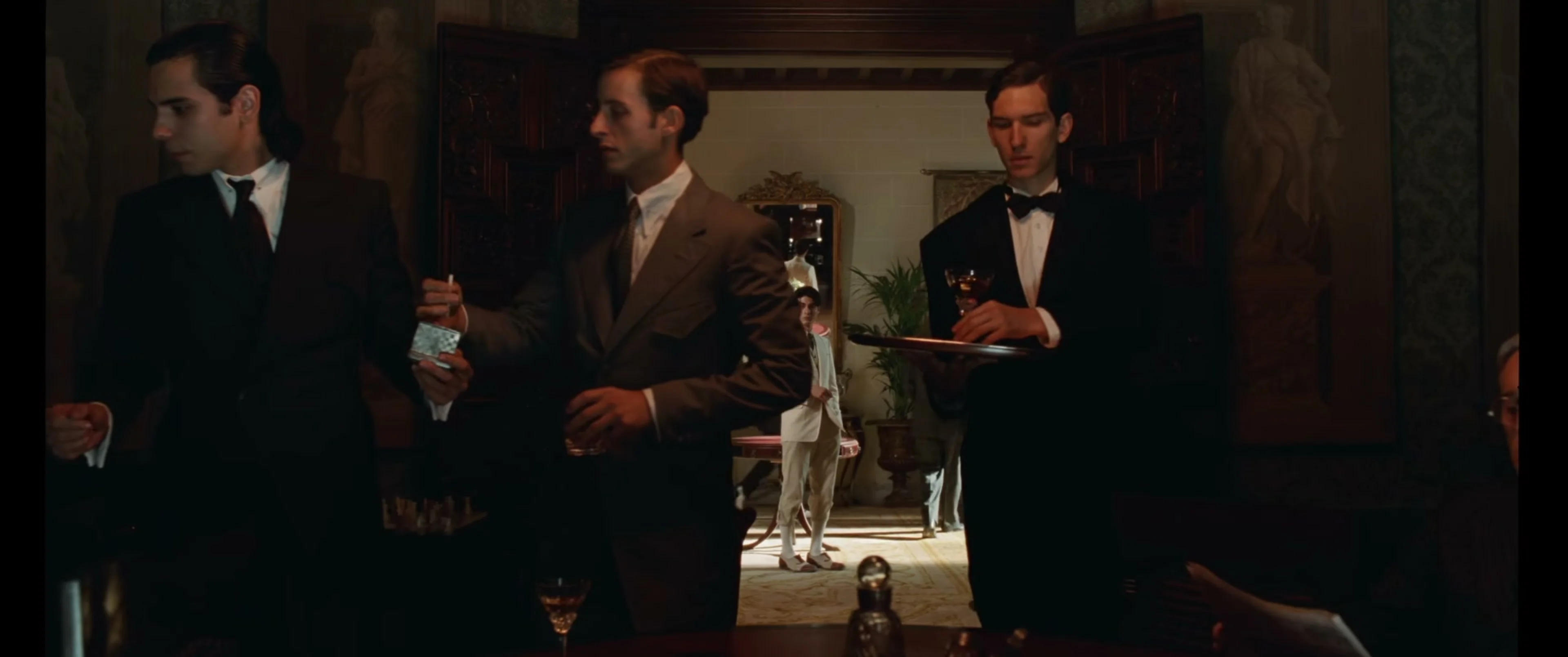 Men in formal clothes watch a performer at an elegant gathering in La Bola Negra.