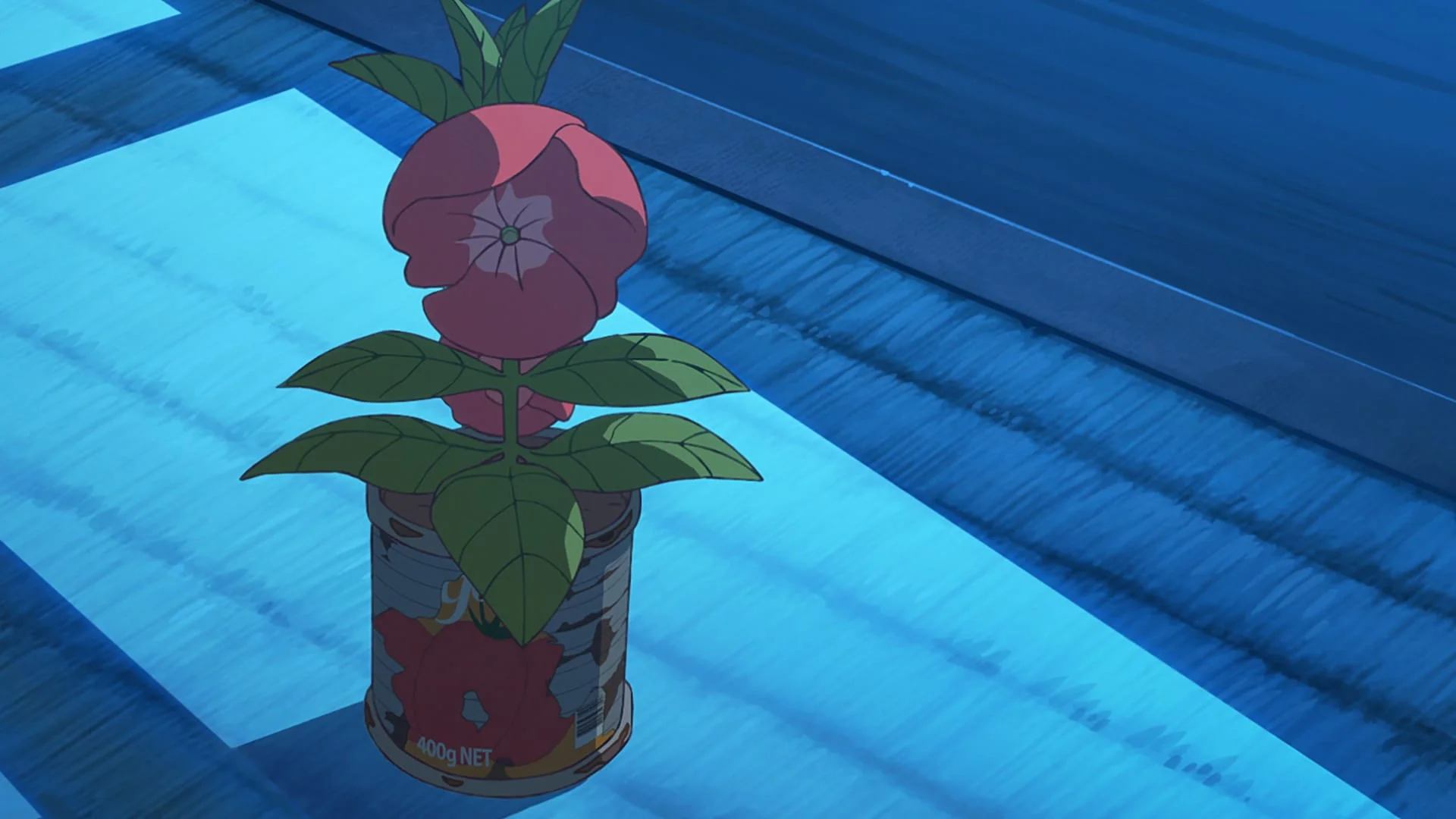 A red balsam flower grows from a metal can on a prison floor.