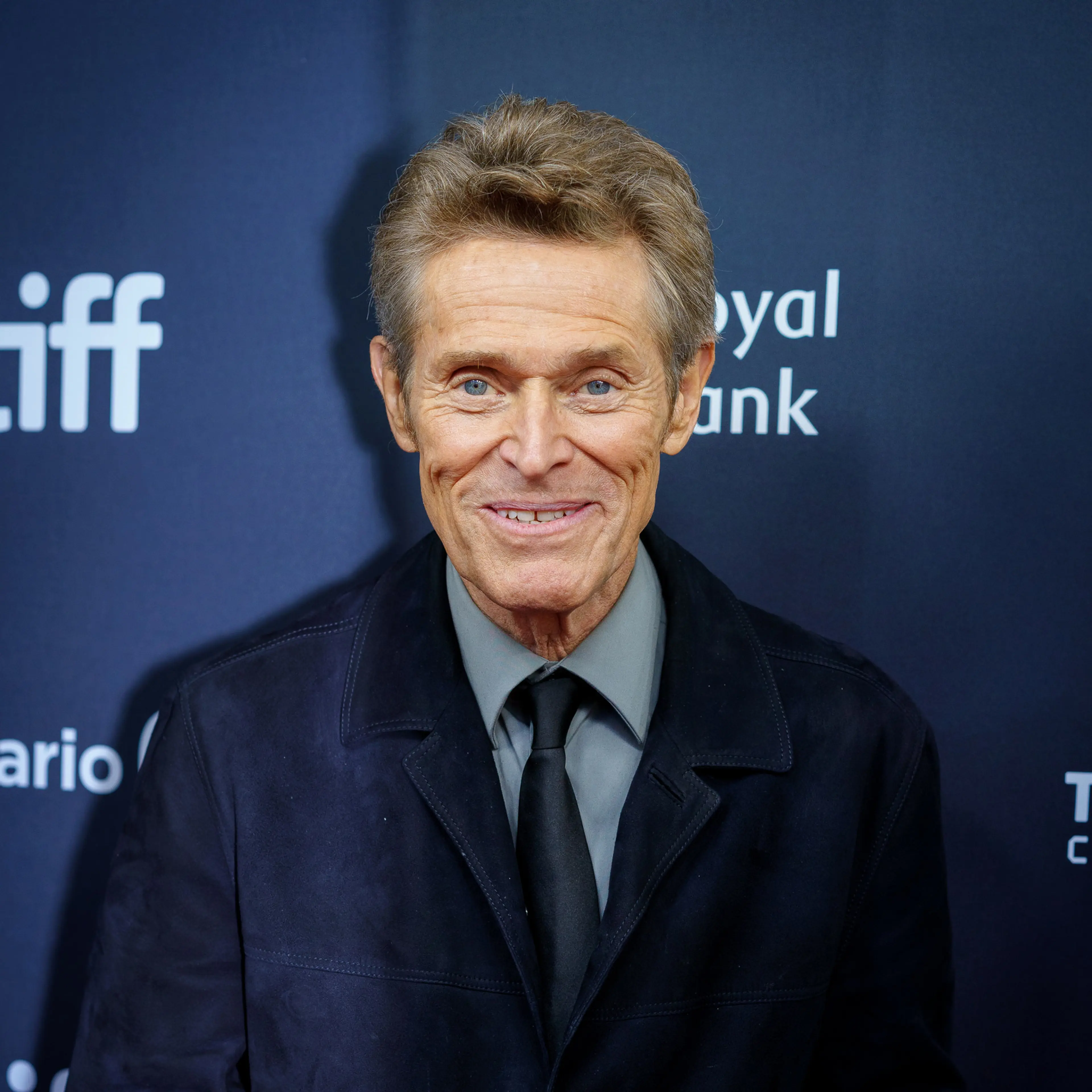 Willem Dafoe smiles on the 2024 Toronto International Film Festival red carpet.