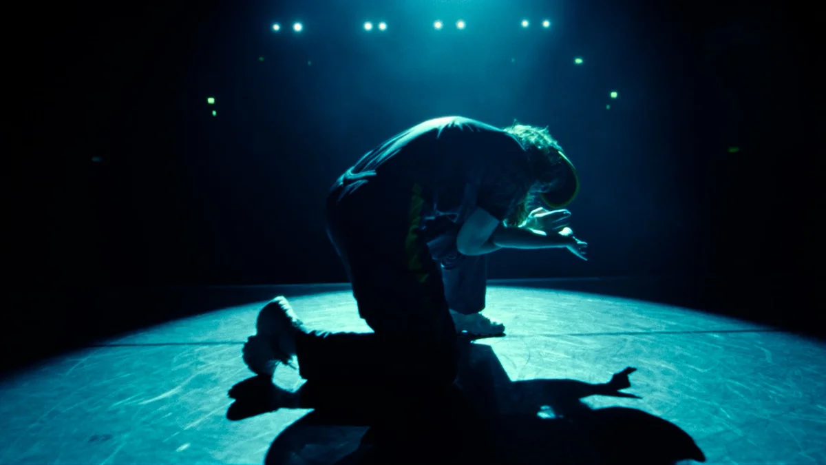 Rachael Gunn crouches on the dance floor beneath bright blue stage lights in an official Netflix image.