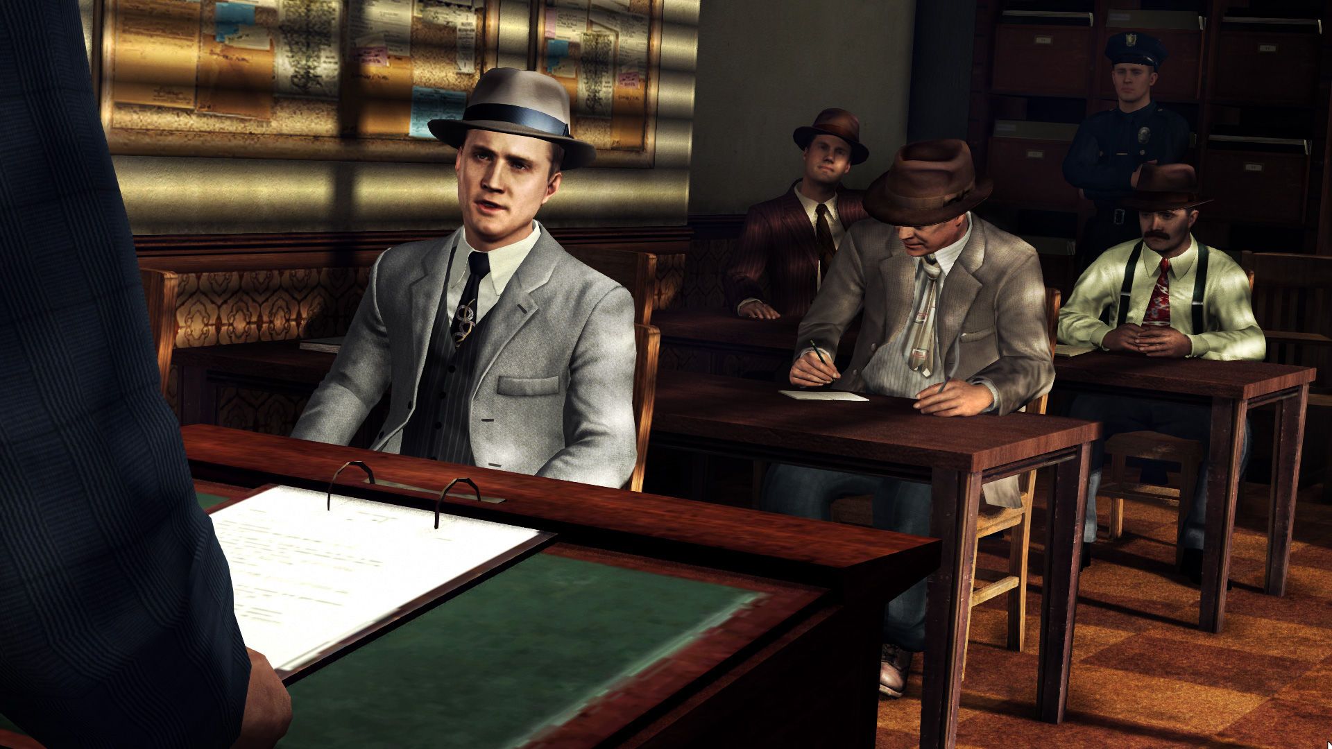 Phelps and other suited officers sit at desks during a police briefing.