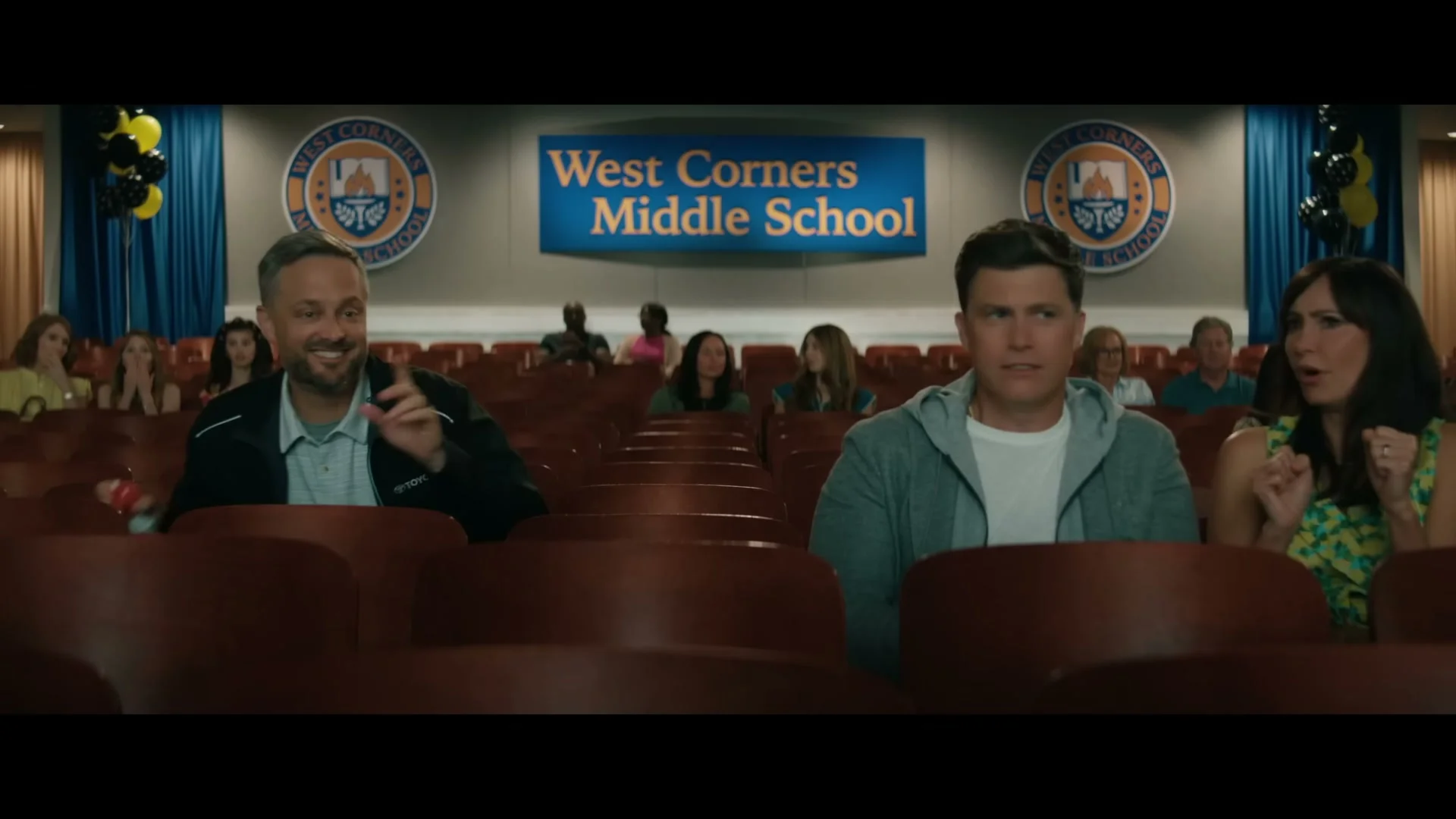 Nate and another father sit beside each other in a school auditorium.