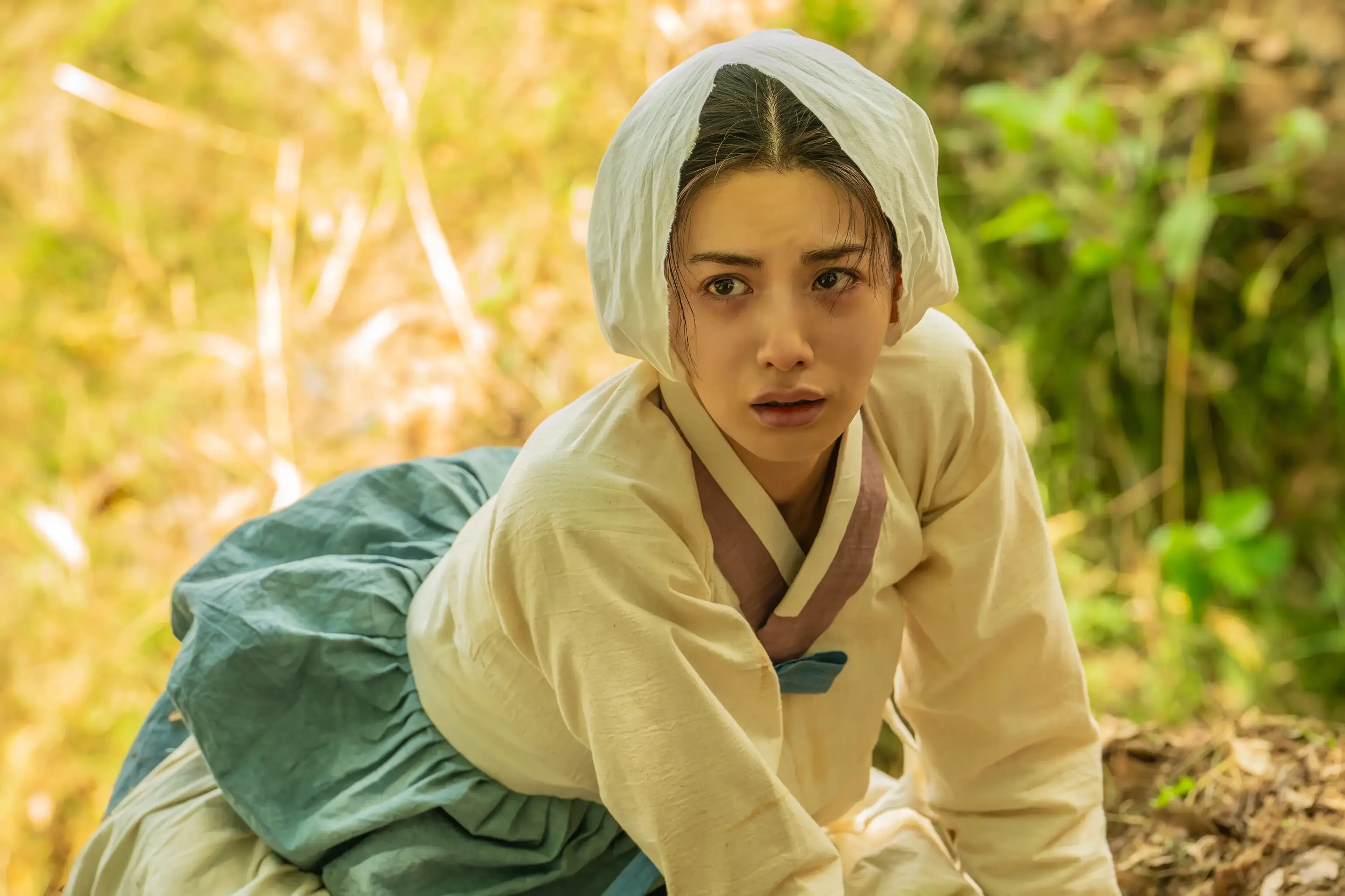 Hui-yeon looks up in a bamboo grove with a pale cloth over her head.