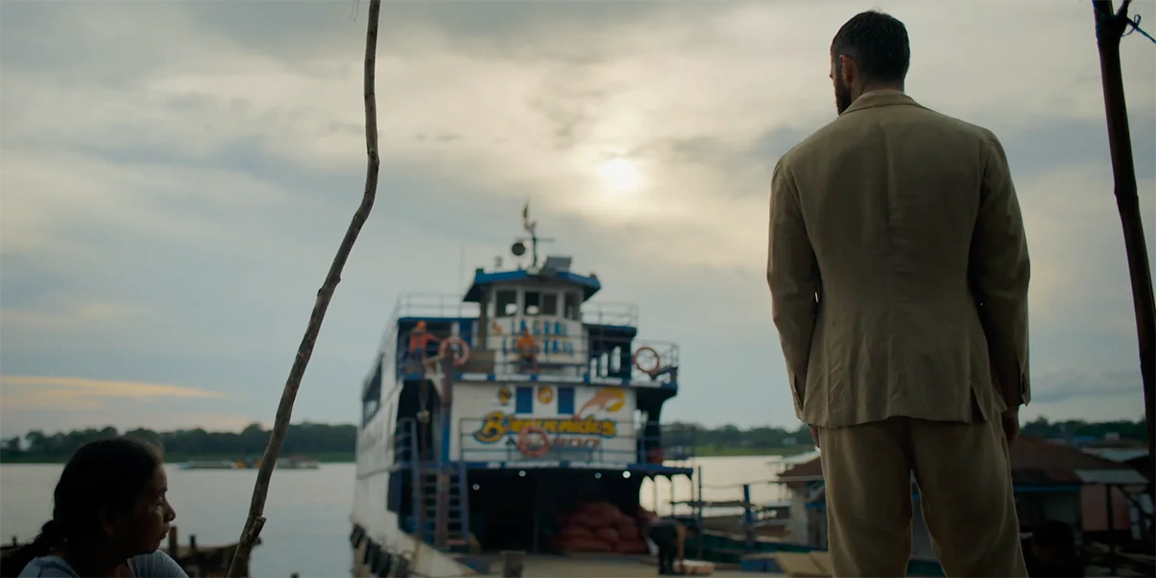Stuart Martin as Ethan Black stands with his back to the camera near a riverboat in The Last Photograph.