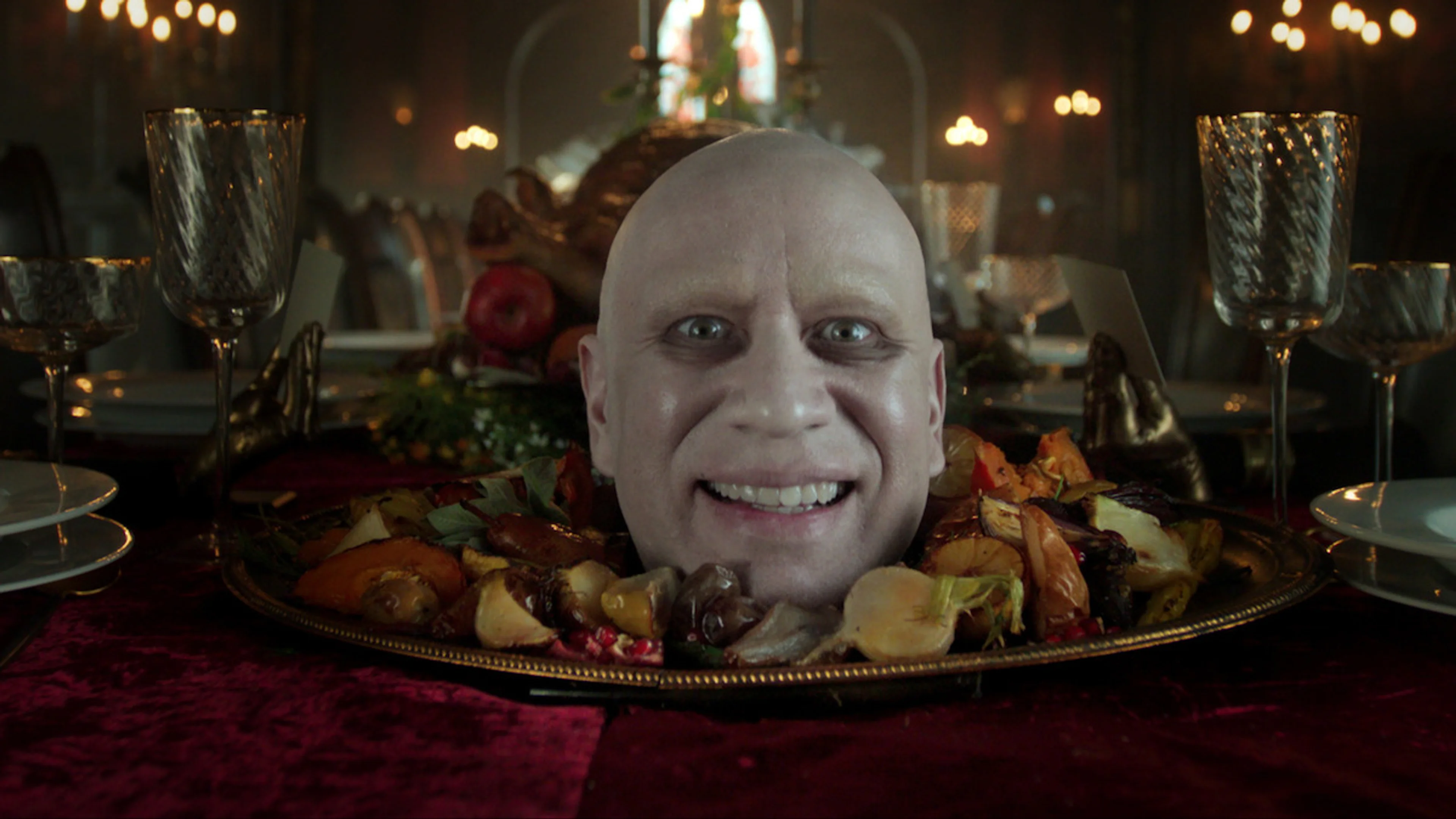 Wednesday Season 3 cast members sit at a dark banquet table with a theatrical platter at the center.