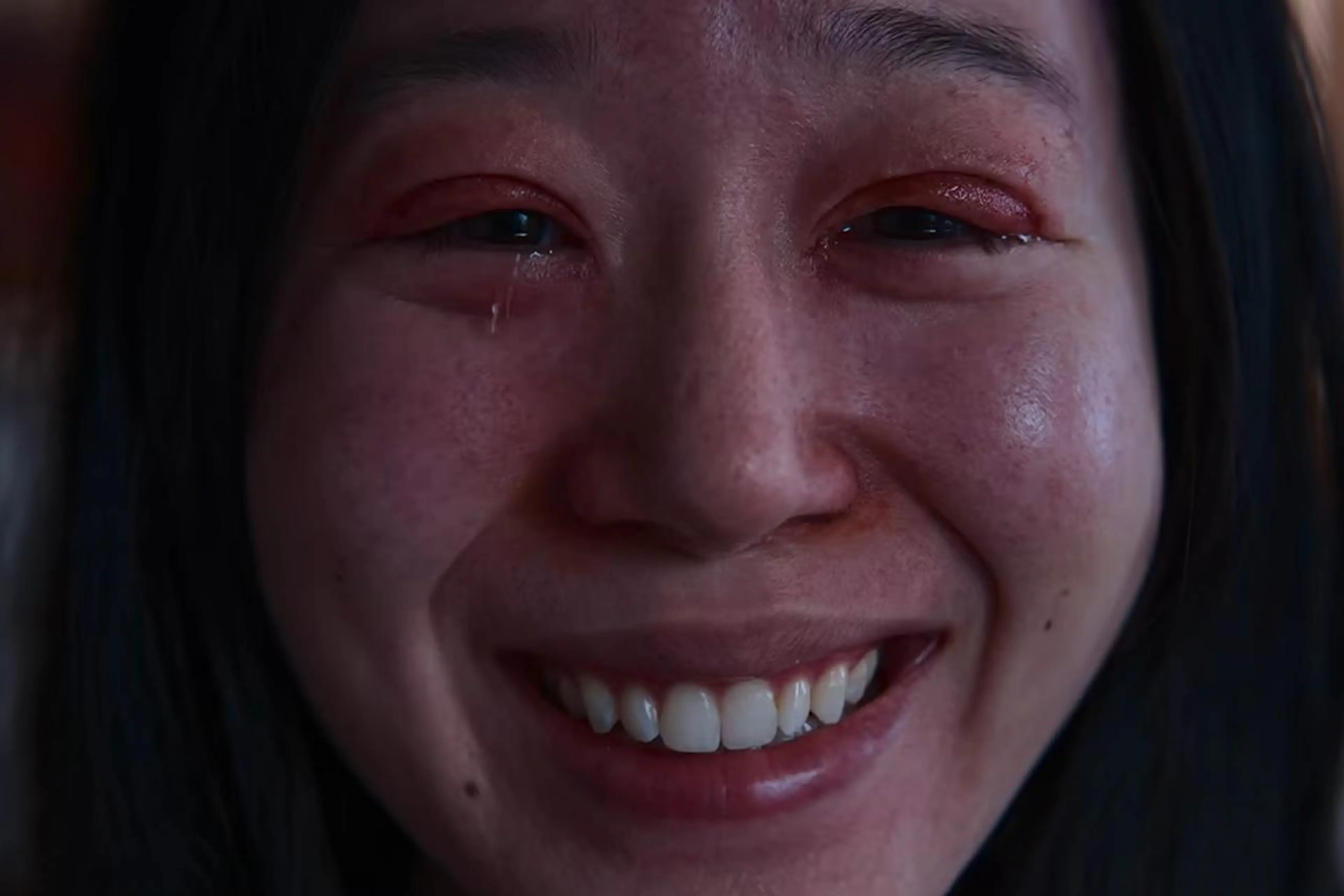 Hana Amano as Yoshiko Tanaka looks tearful in a close-up with bruising around her eyes.