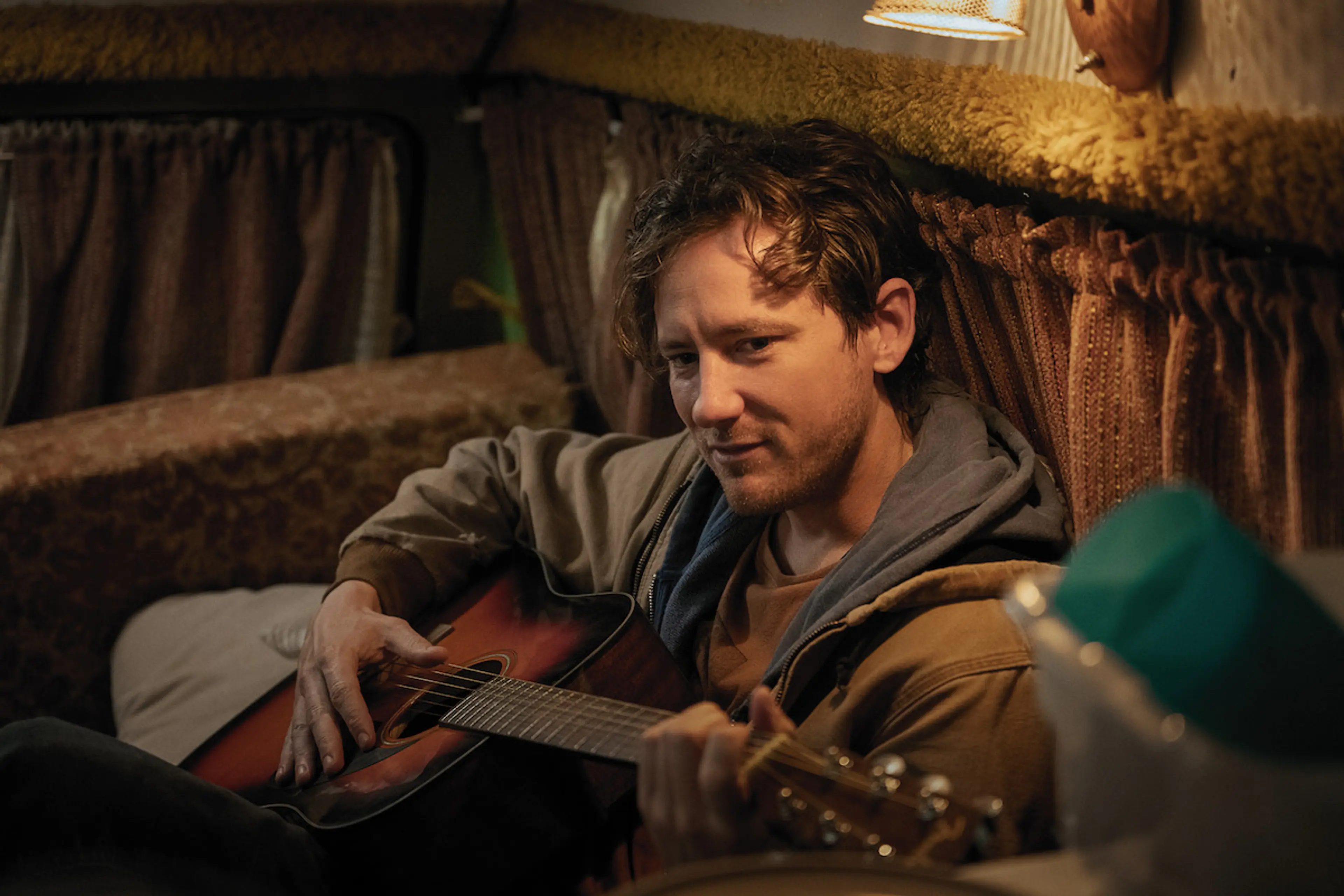 Lewis Pullman as Cameron sits in a van with a guitar, with his face clearly visible.