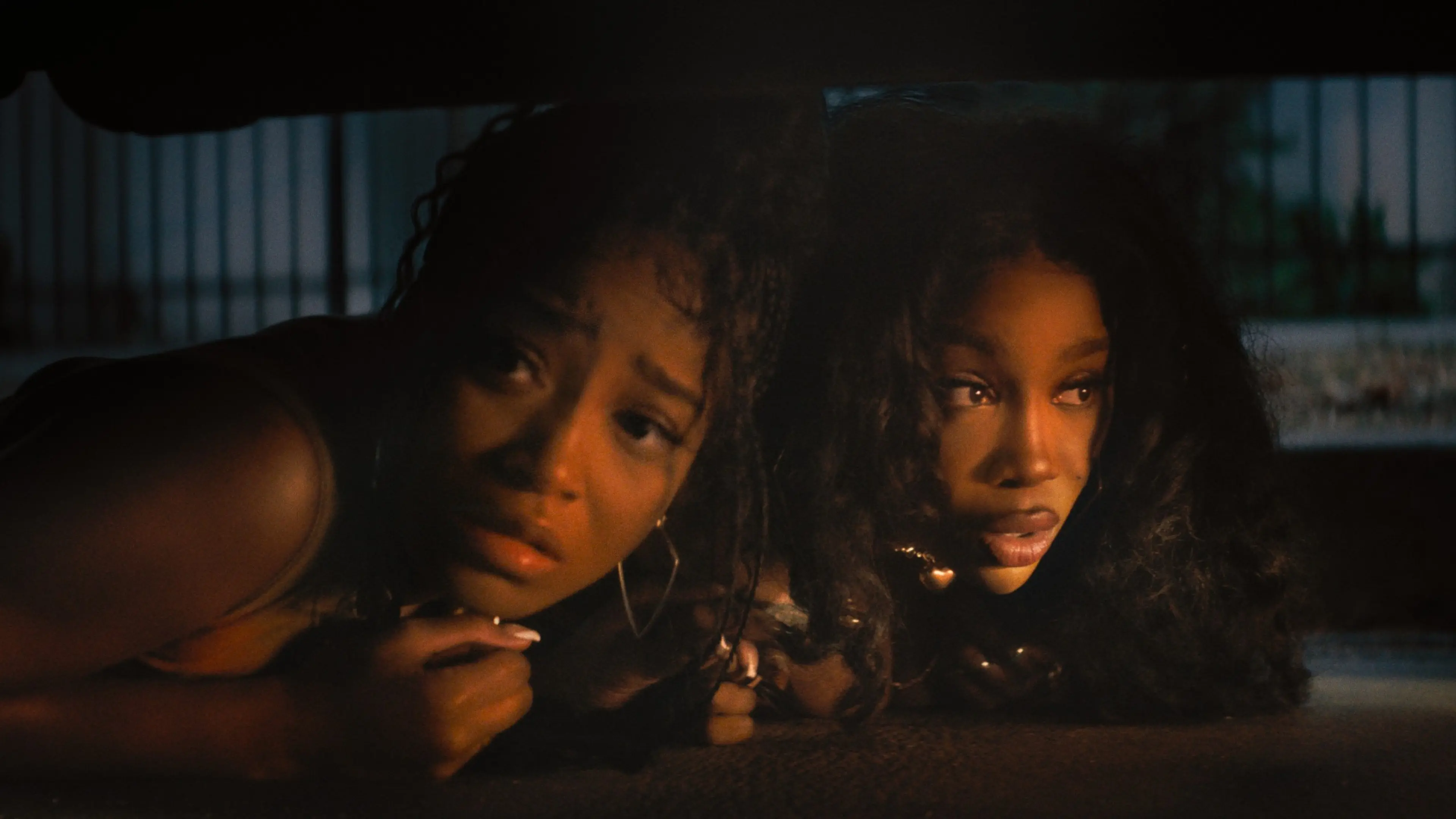 Keke Palmer and SZA crouch close together in a dimly lit outdoor space.