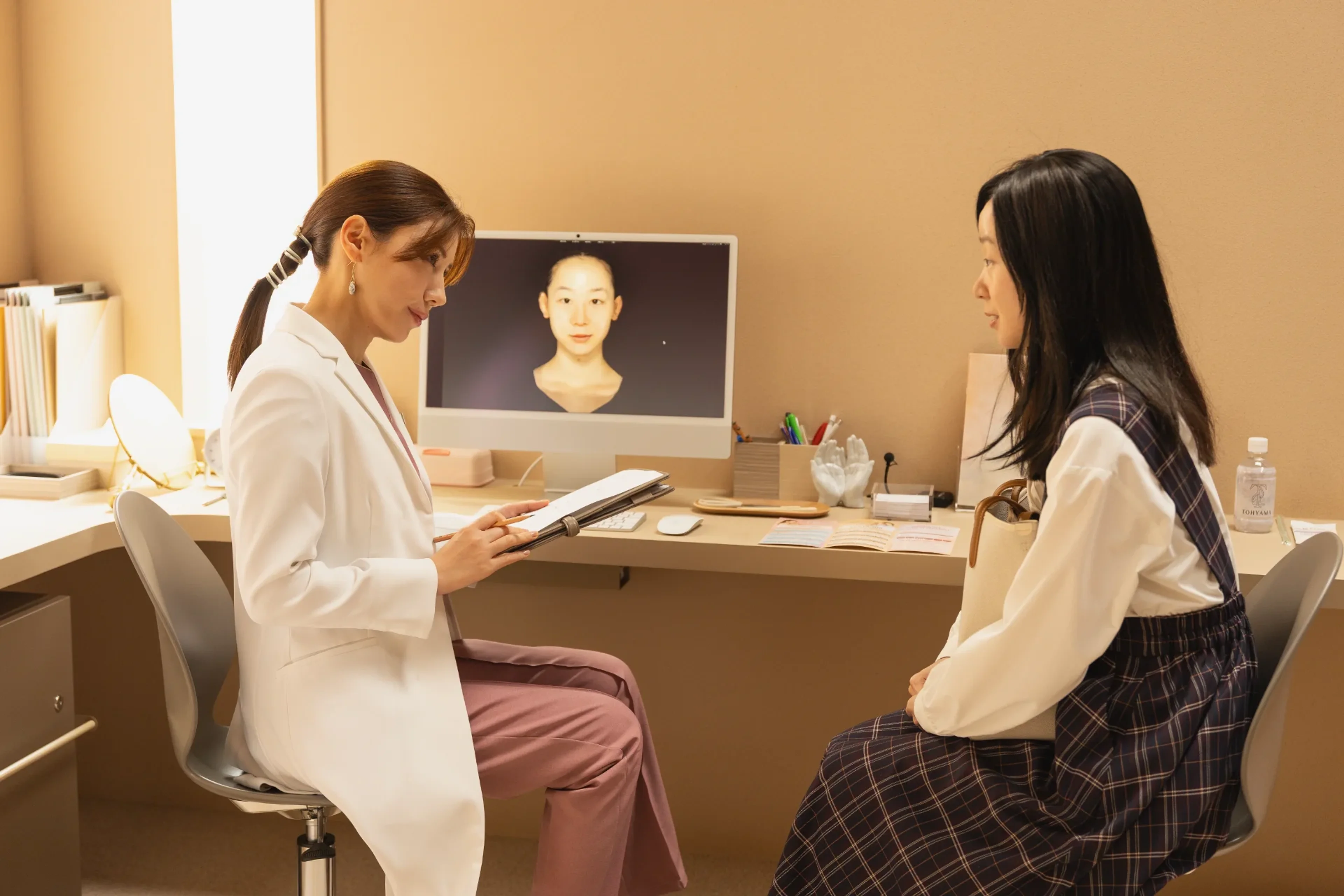 A doctor speaks with a young woman beside a computer displaying the patient's portrait.