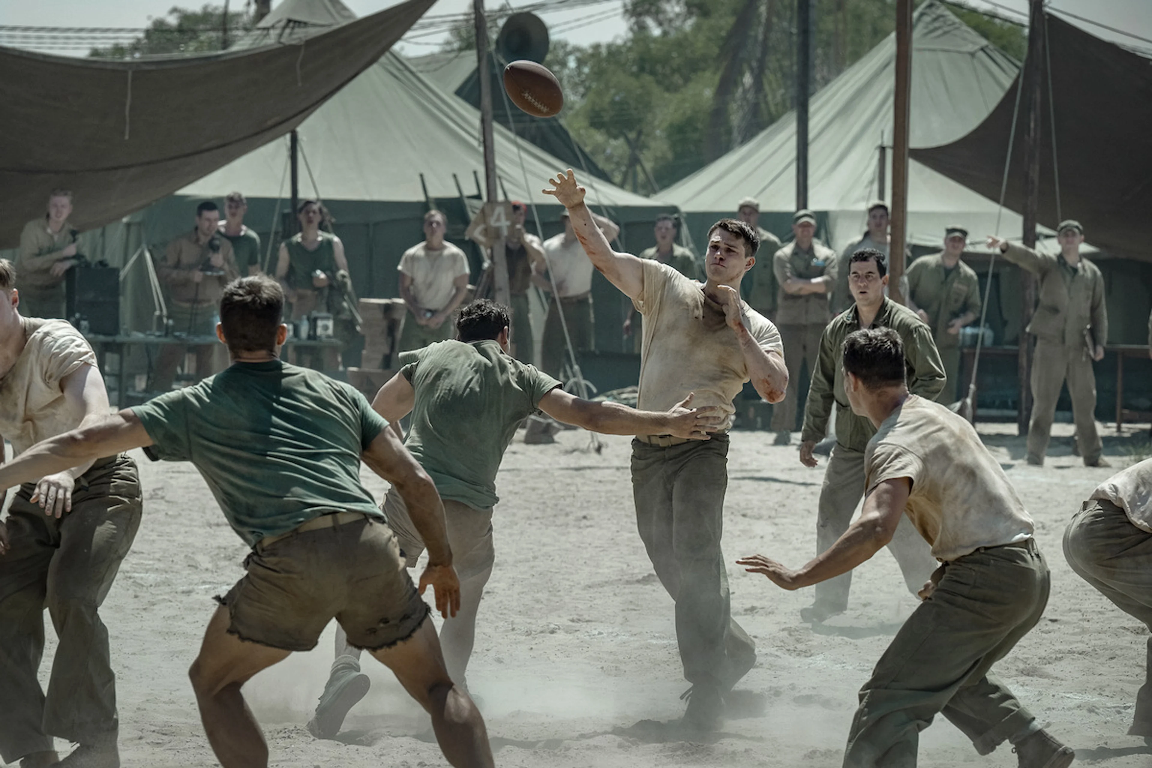 Nicholas Galitzine as John McLaughry carries a football while Marines watch from the sideline in The Mosquito Bowl.