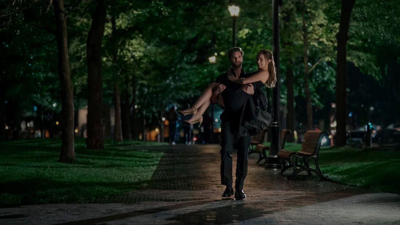 Lili Reinhart and Tom Bateman appear together in a nighttime park scene from The Love Hypothesis.