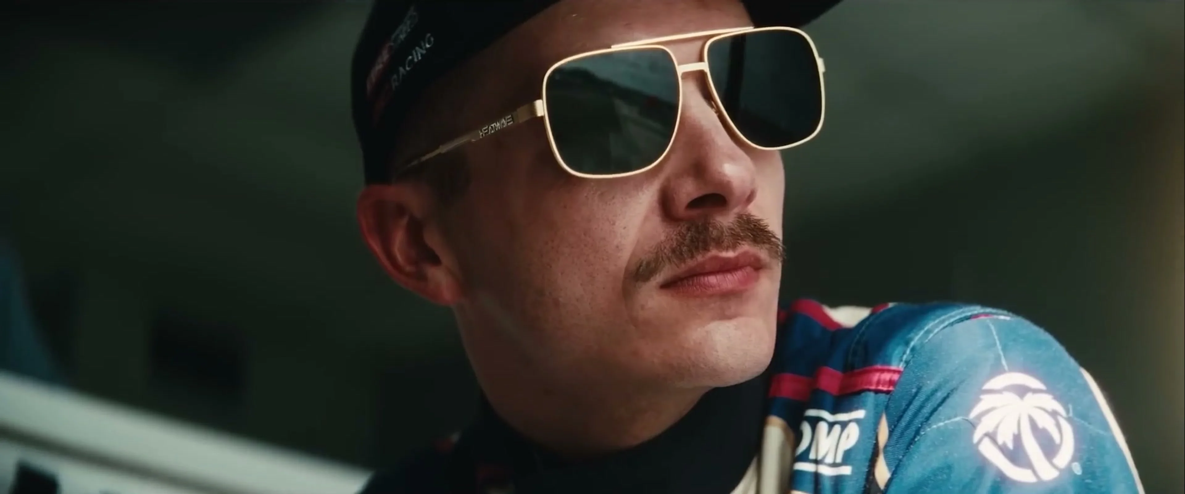 A man in a blue racing suit and sunglasses watches the track in Drifter.