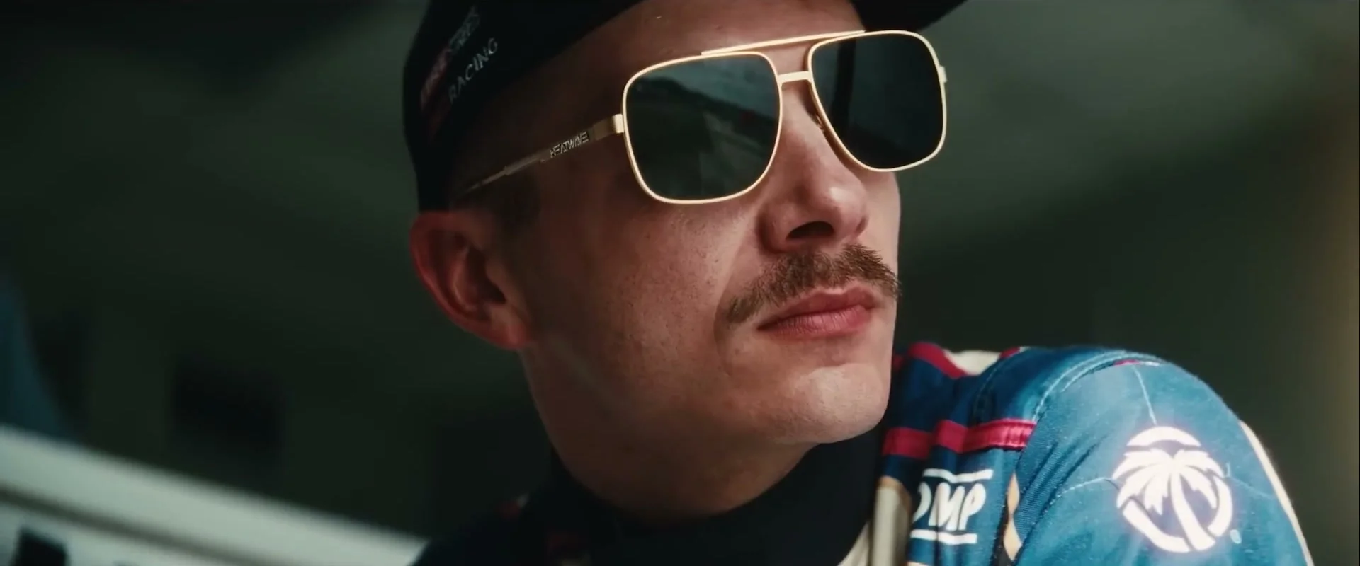 A man in a blue racing suit and sunglasses watches the track in Drifter.