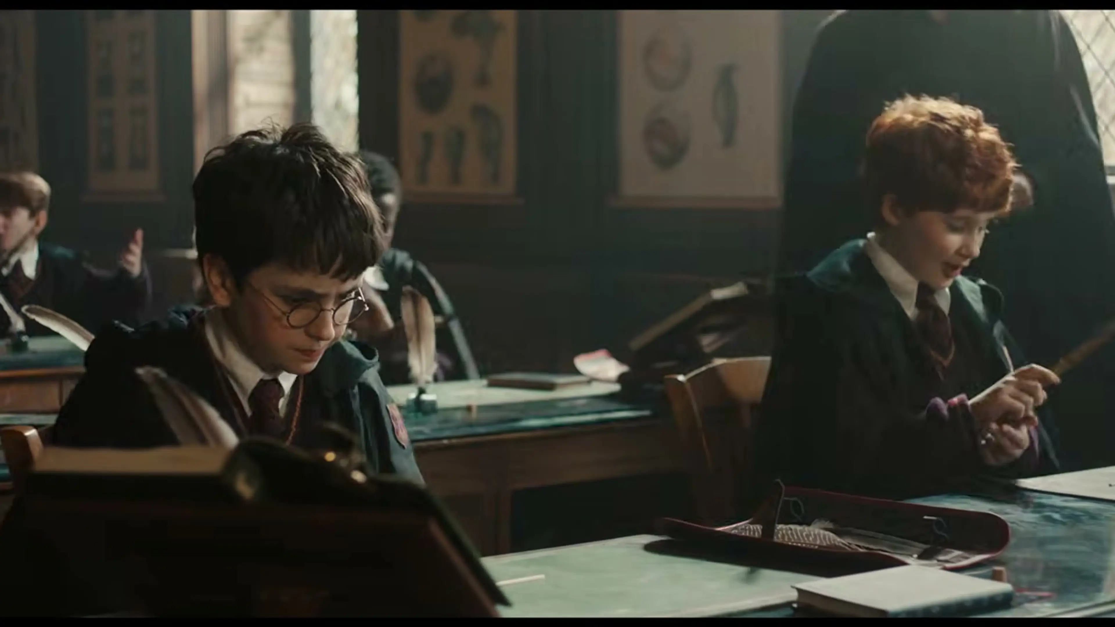 Harry Potter and Ron Weasley sit at wooden desks during a Hogwarts lesson.