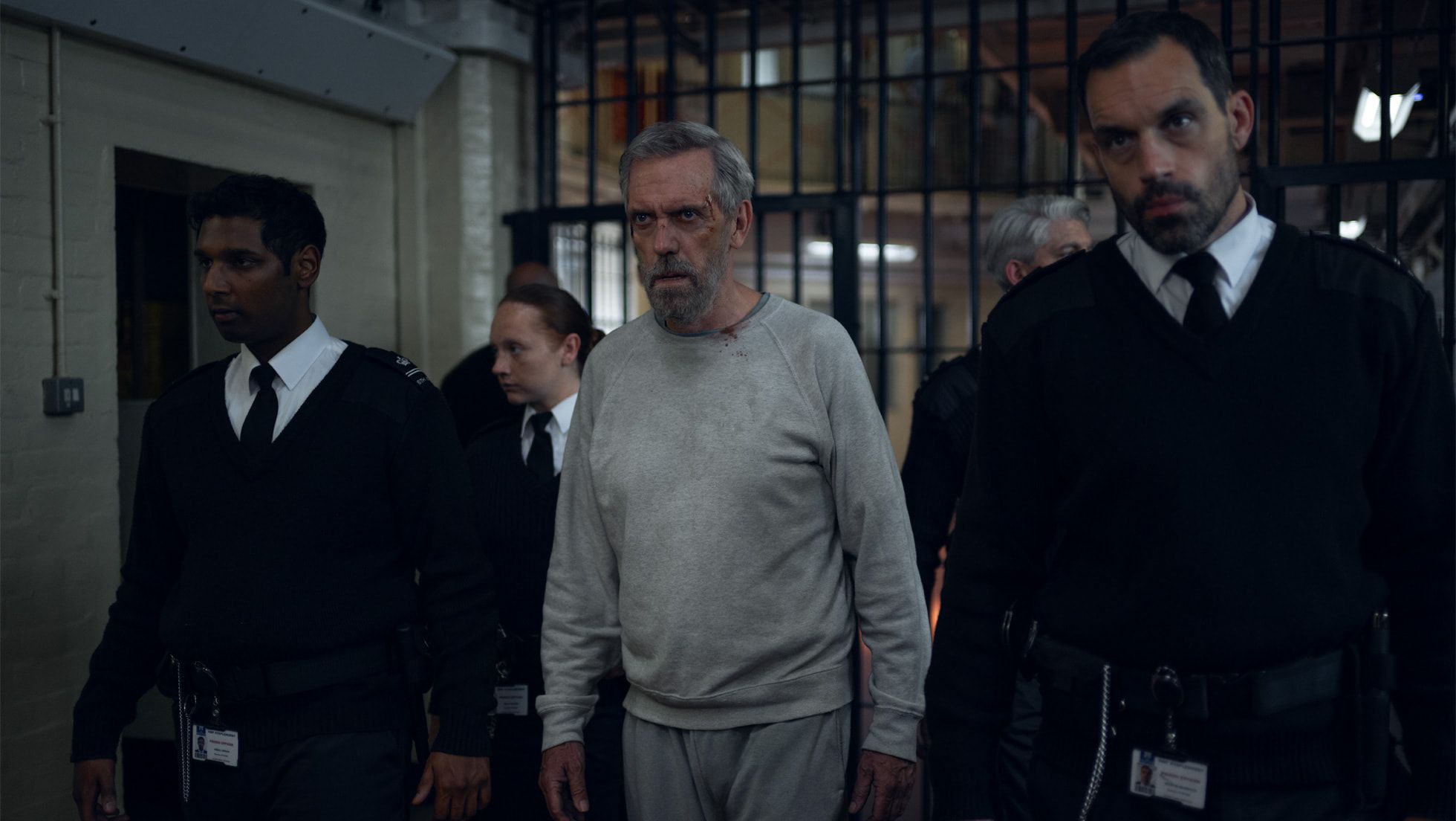 Hugh Laurie as Felix Carmichael walks through a prison corridor with guards in The Wanted Man.