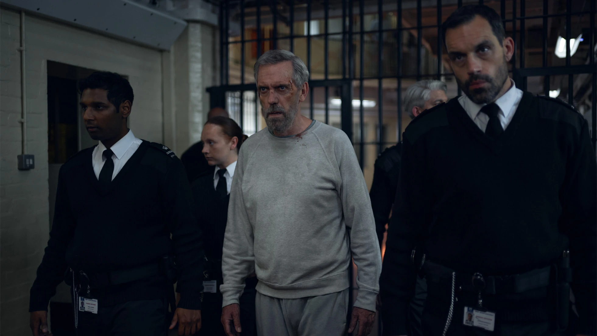 Hugh Laurie as Felix Carmichael walks through a prison corridor with guards in The Wanted Man.