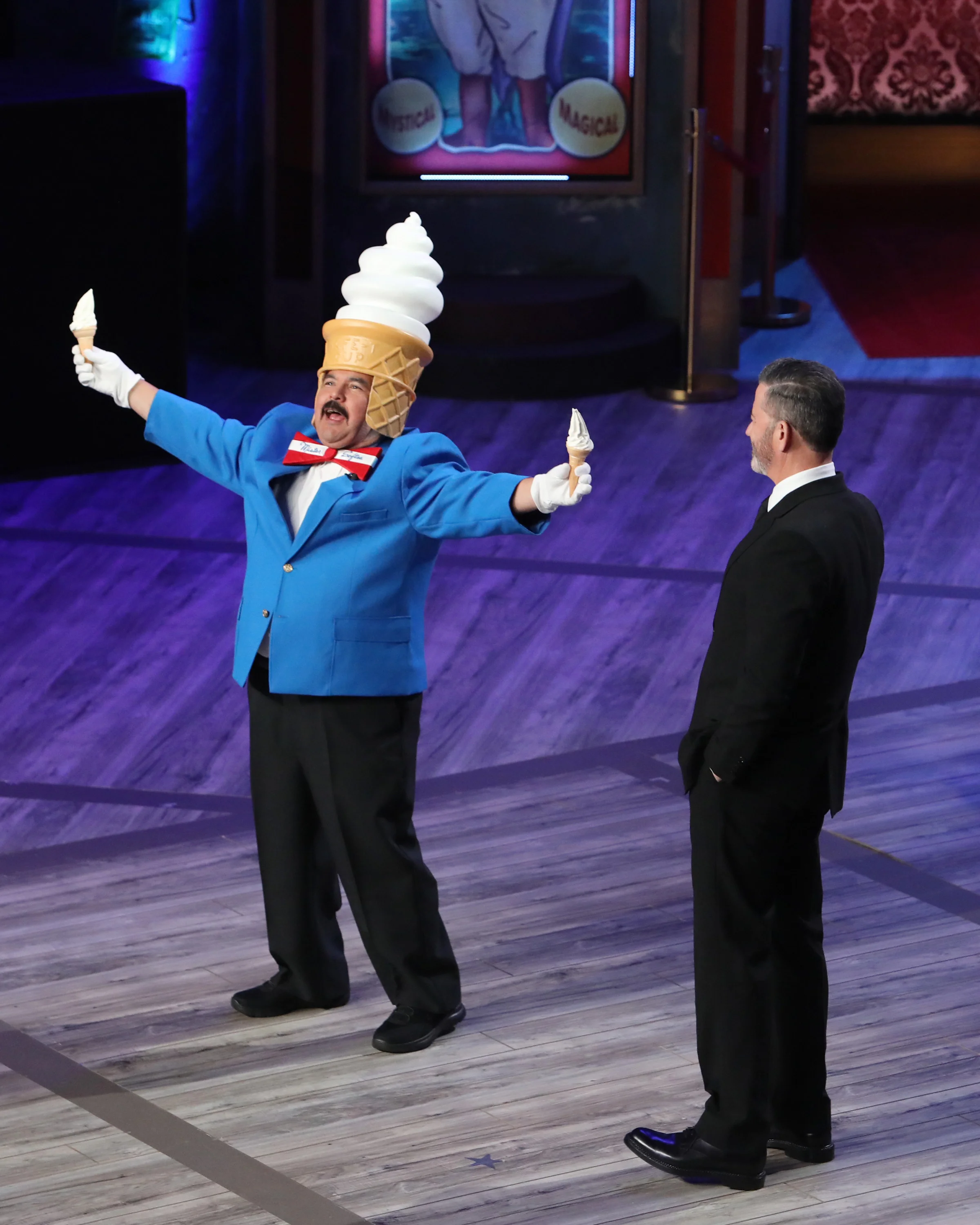 Guillermo holds an ice-cream cone in each hand beside Jimmy Kimmel.