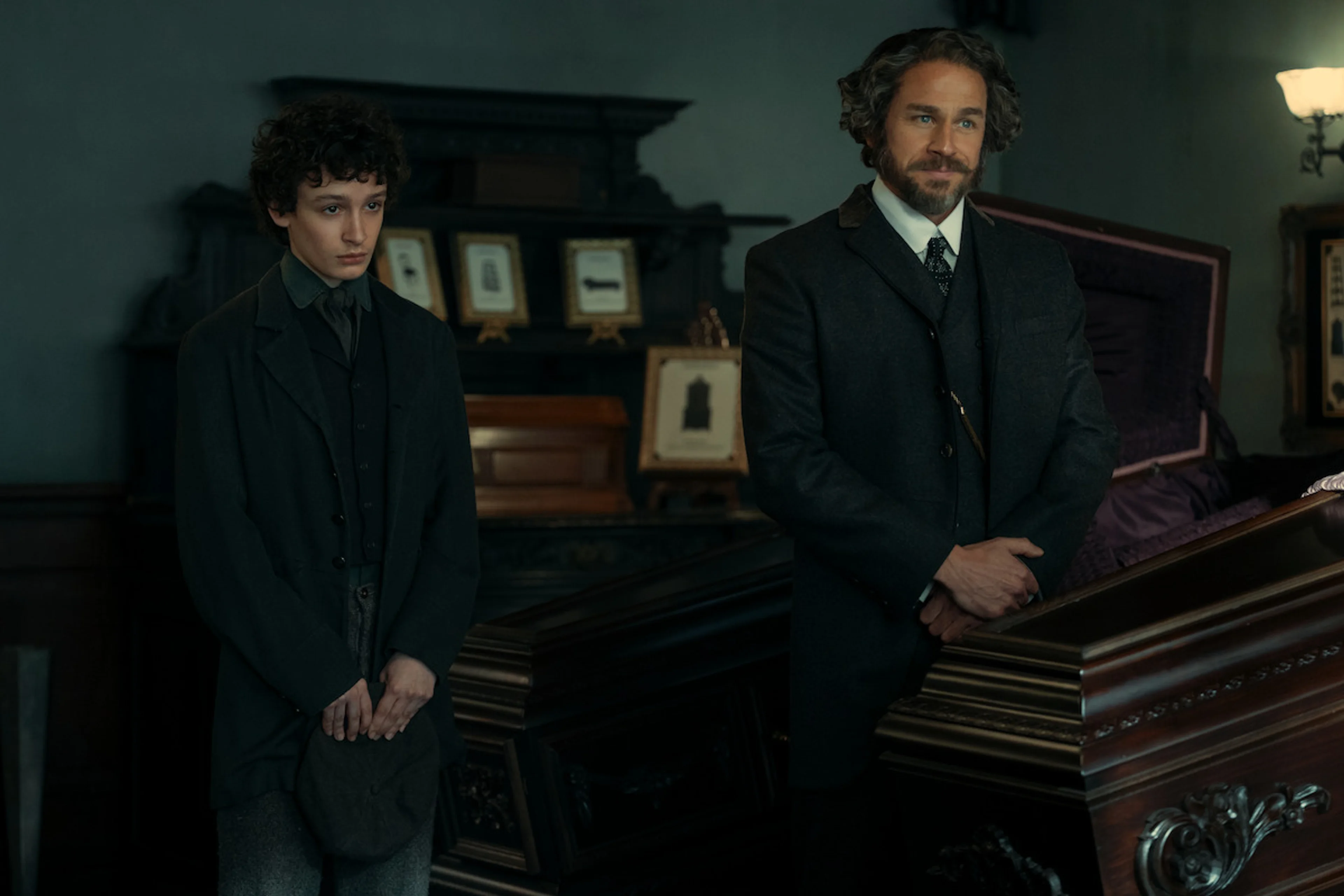 Two figures stand beside a coffin in a period scene from Monster: The Lizzie Borden Story.