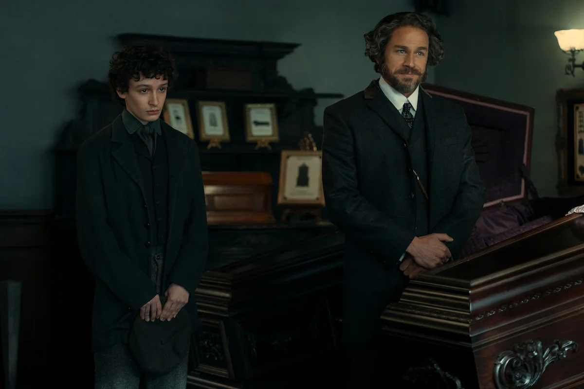 Two figures stand beside a coffin in a period scene from Monster: The Lizzie Borden Story.