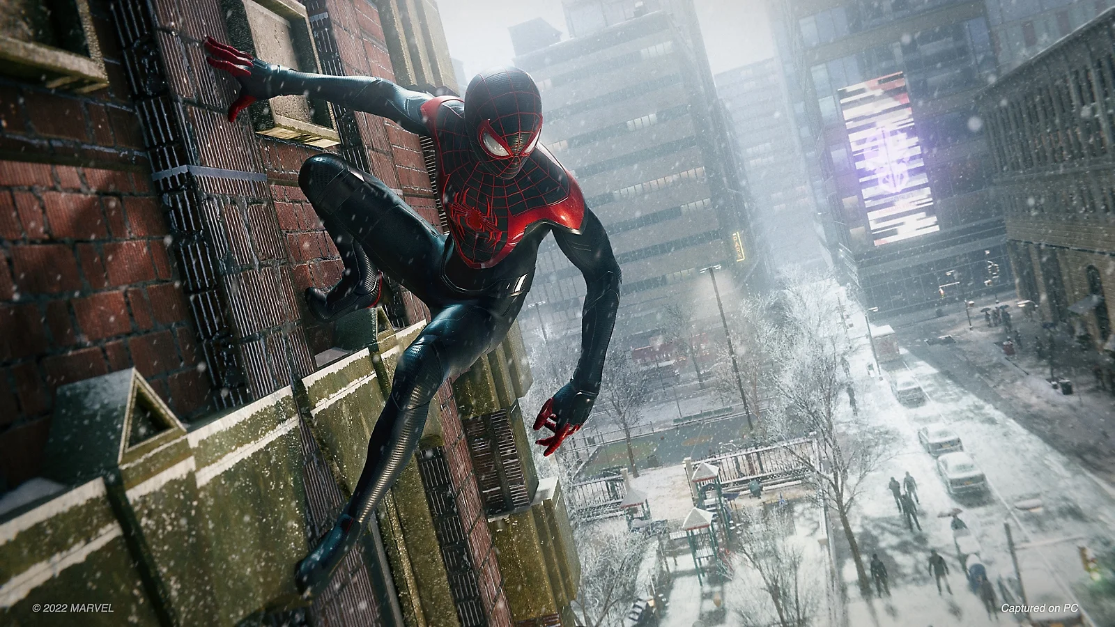 Miles Morales in his black and red Spider-Man suit clings to a snowy building in an official PlayStation image.