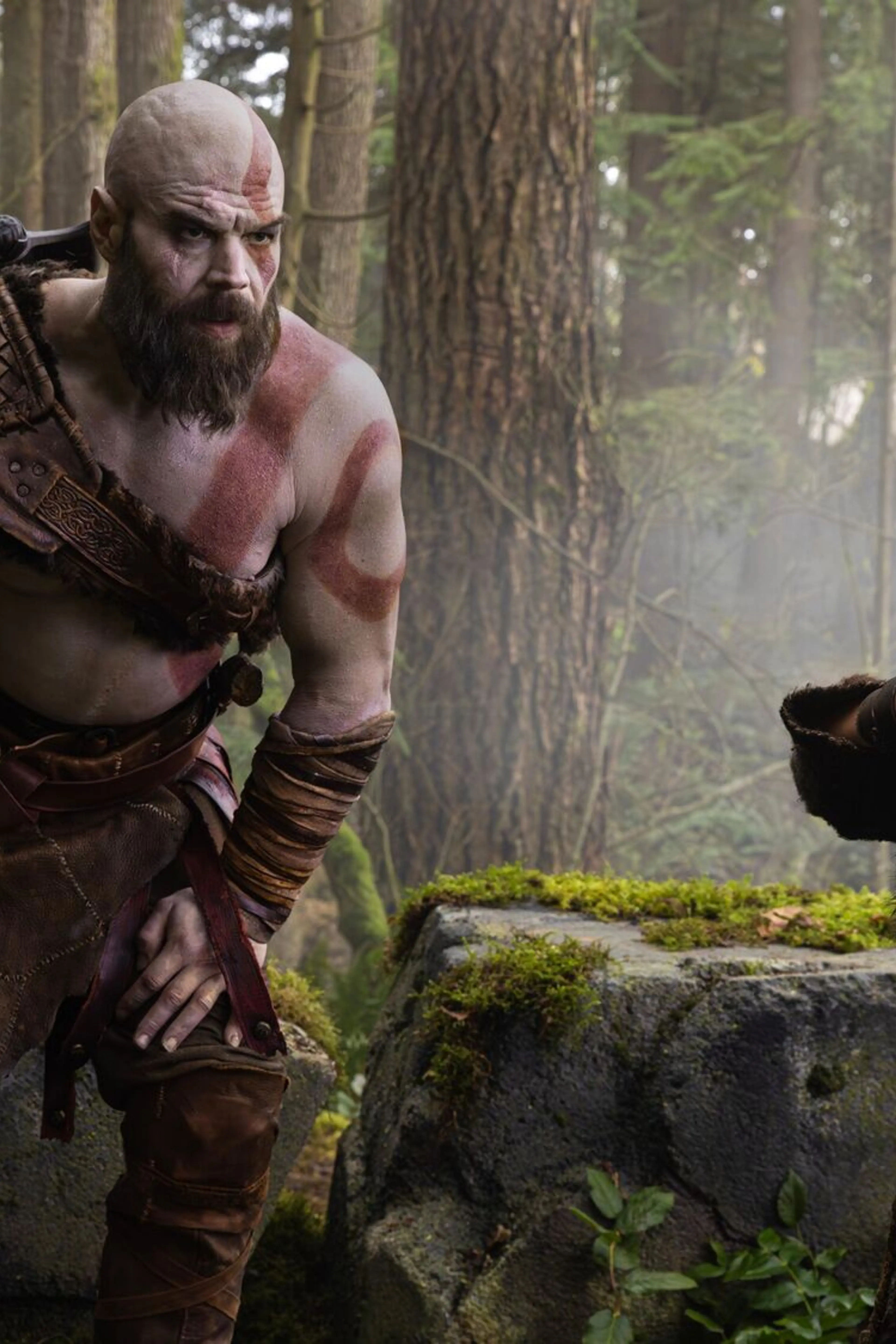 Kratos watches from behind a tree as Atreus aims a bow in Prime Video’s God of War series