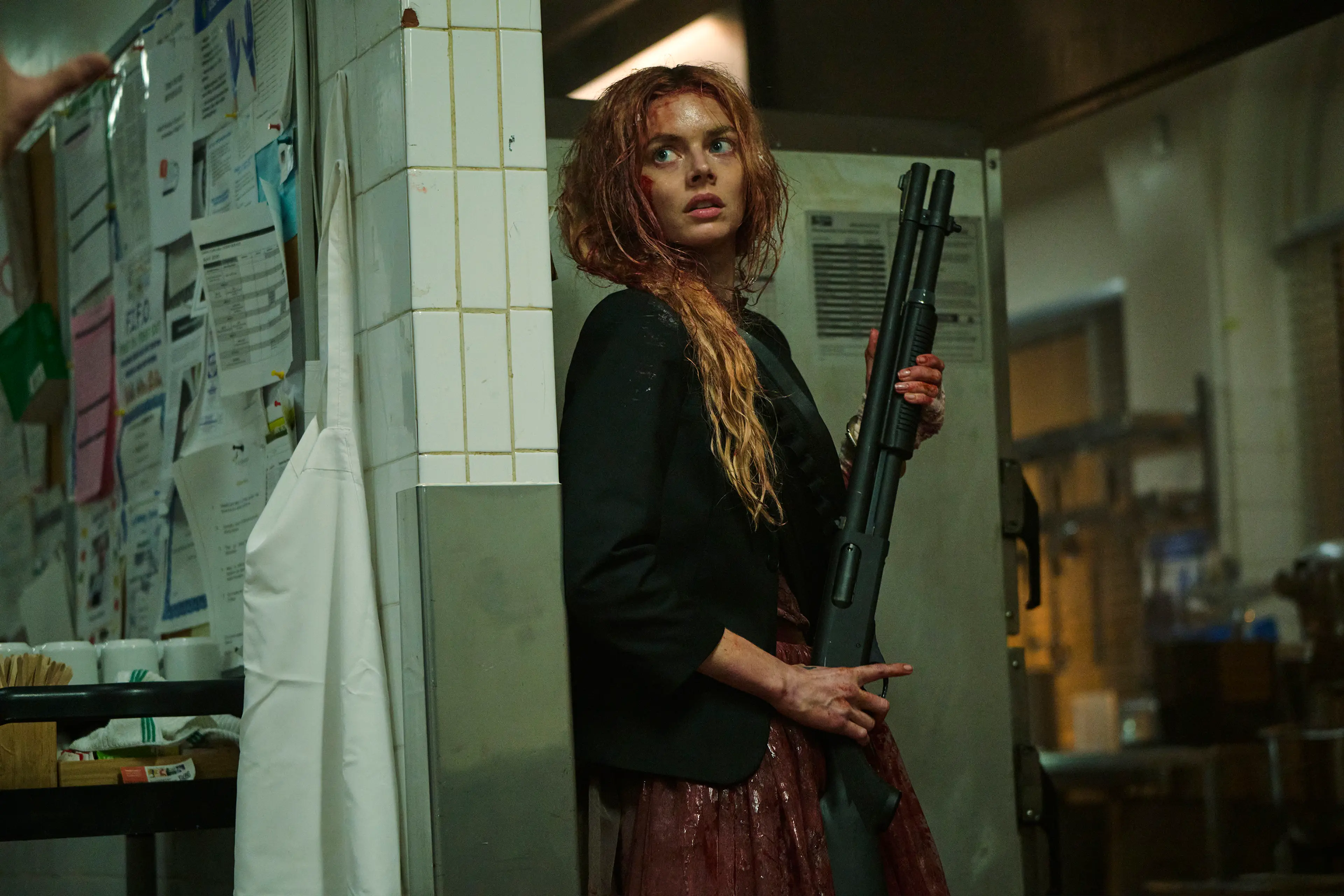Grace holds a shotgun beside a tiled doorway and looks over her shoulder.
