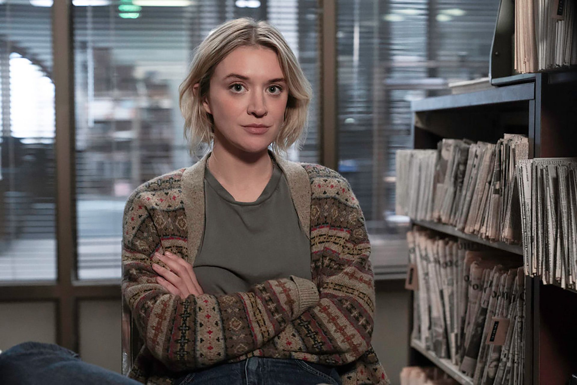 Mare sits in the newsroom wearing a brown jacket over a grey shirt.
