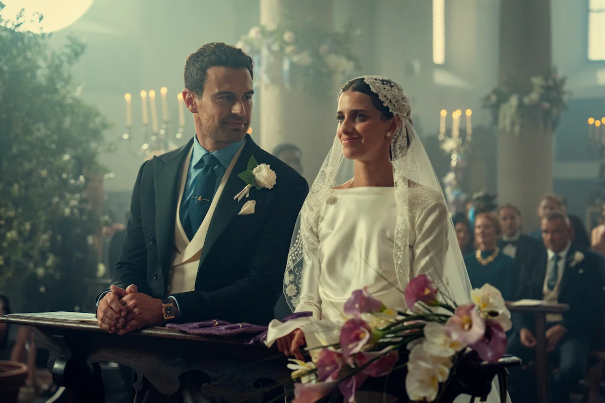 Theo James as Eddie and Benedetta Porcaroli as Bella sit together in wedding clothes inside a decorated church.