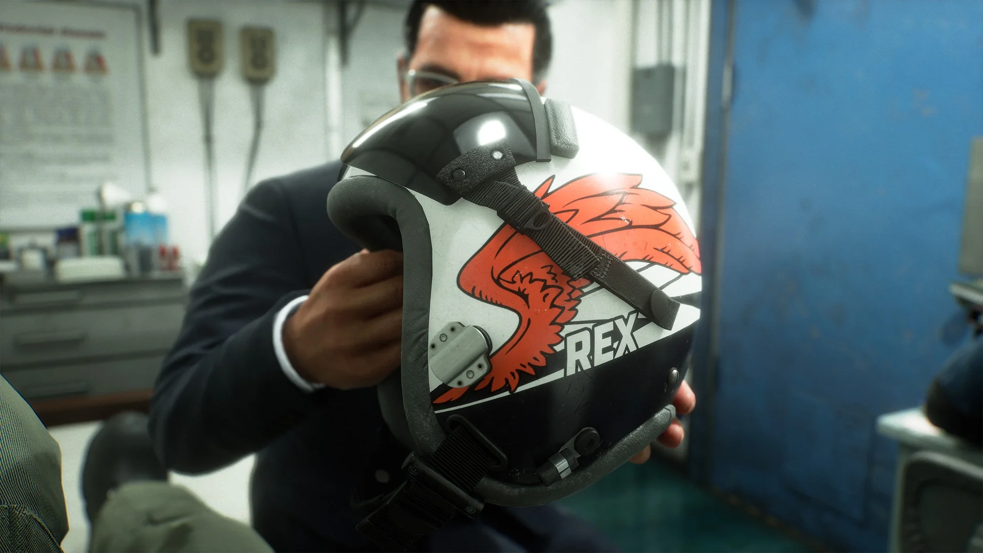 A man holds a marked pilot helmet inside an Ace Combat 8 hangar.