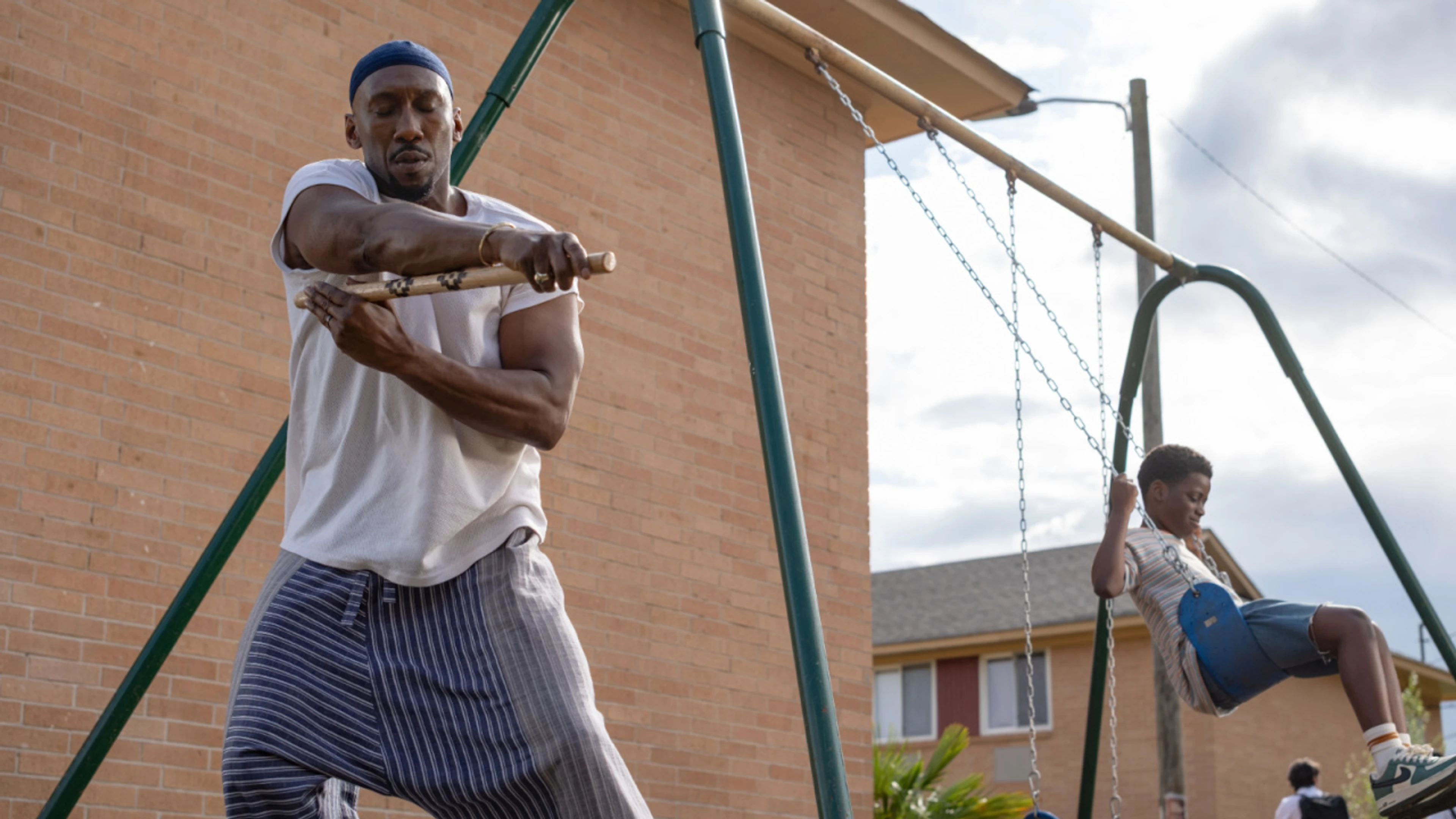 Mahershala Ali as Latif stands near a child on a backyard swing.