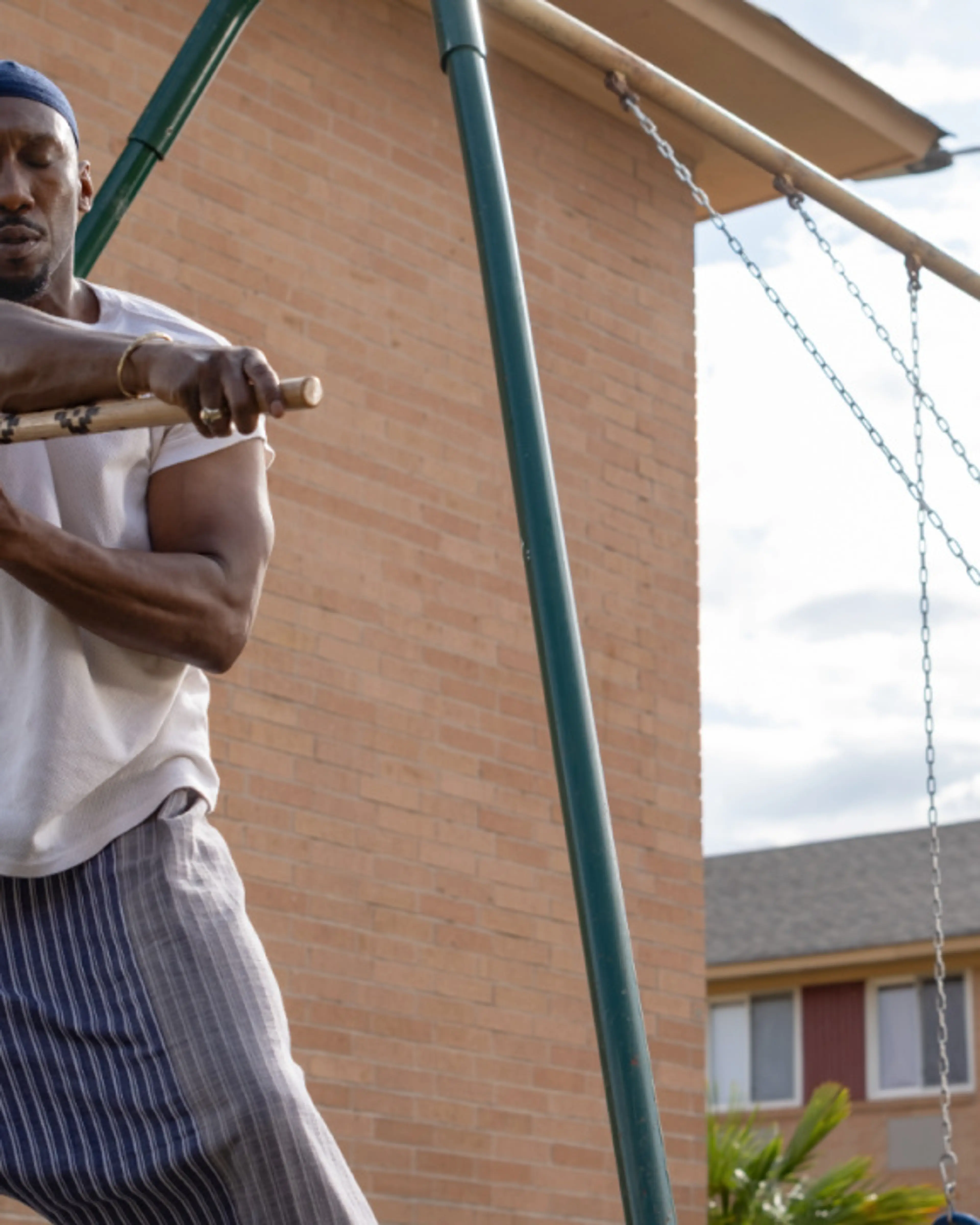 Mahershala Ali as Latif stands near a child on a backyard swing.