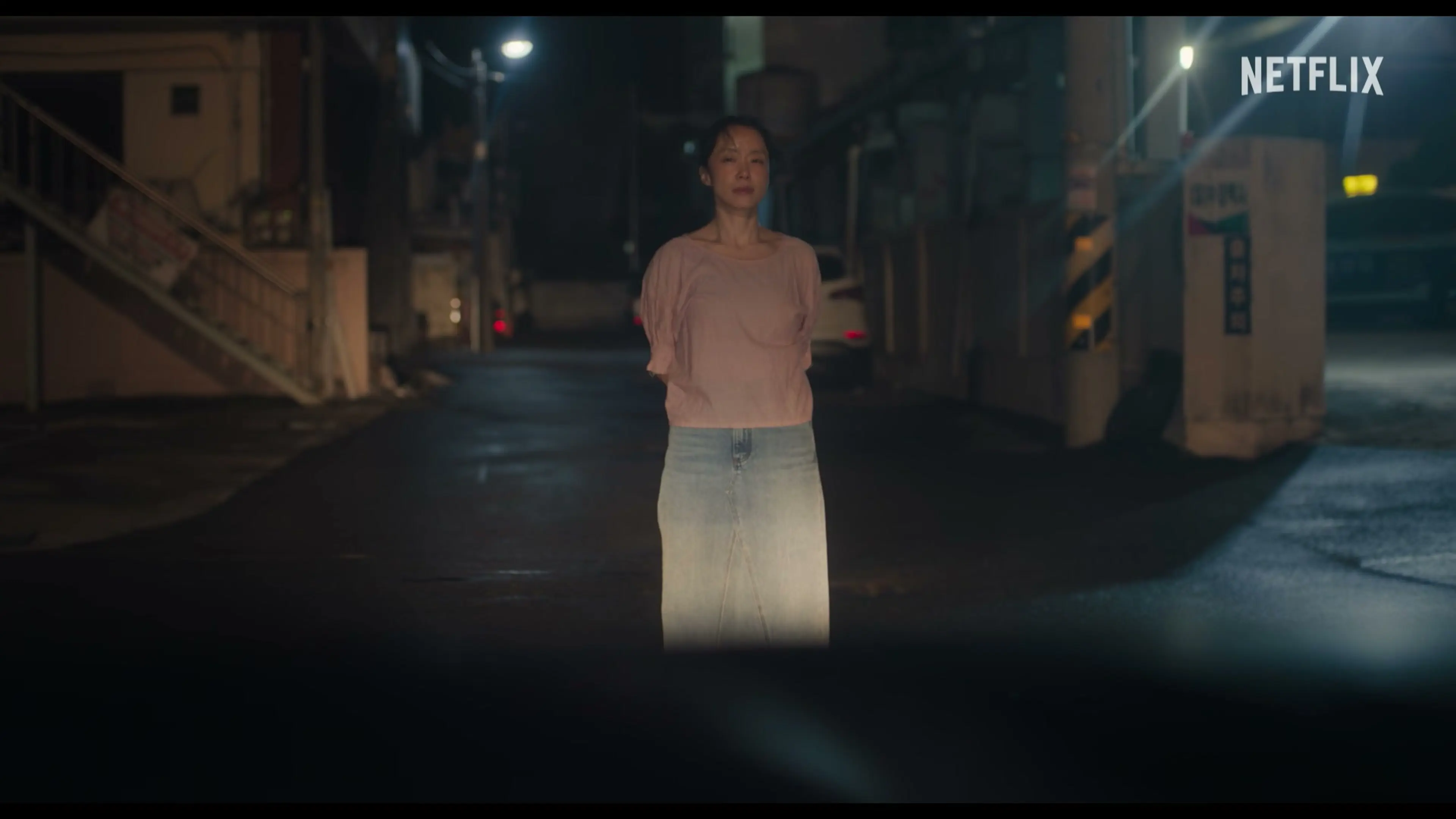 Mi-ok stands in a street at night wearing a pink top and long skirt.
