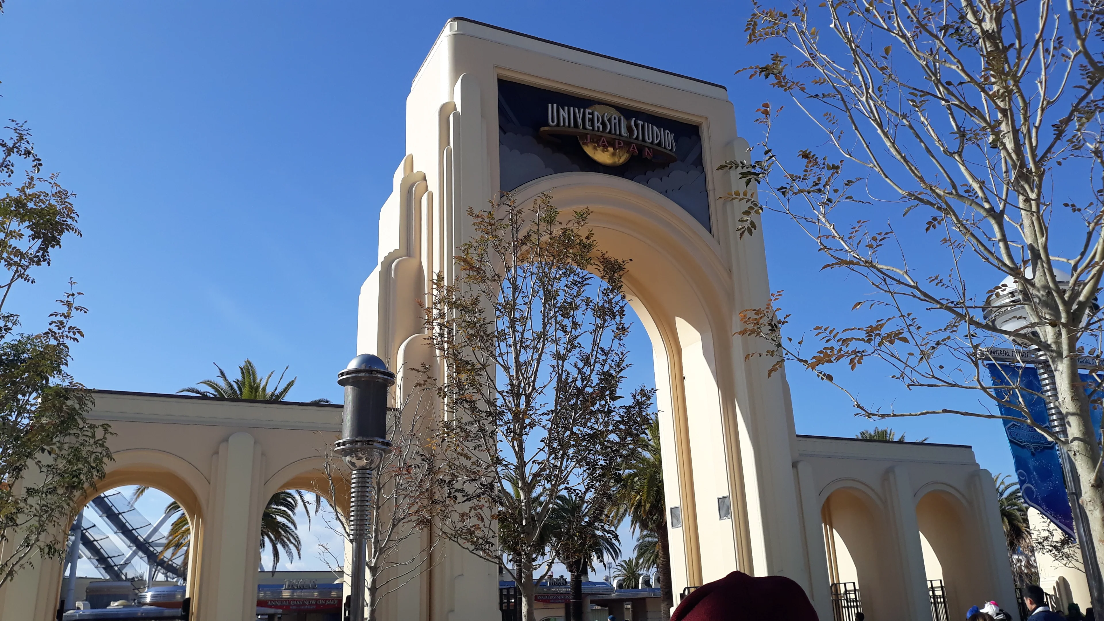 The cream-colored Universal Studios Japan entrance arch stands against a clear blue sky in Osaka.