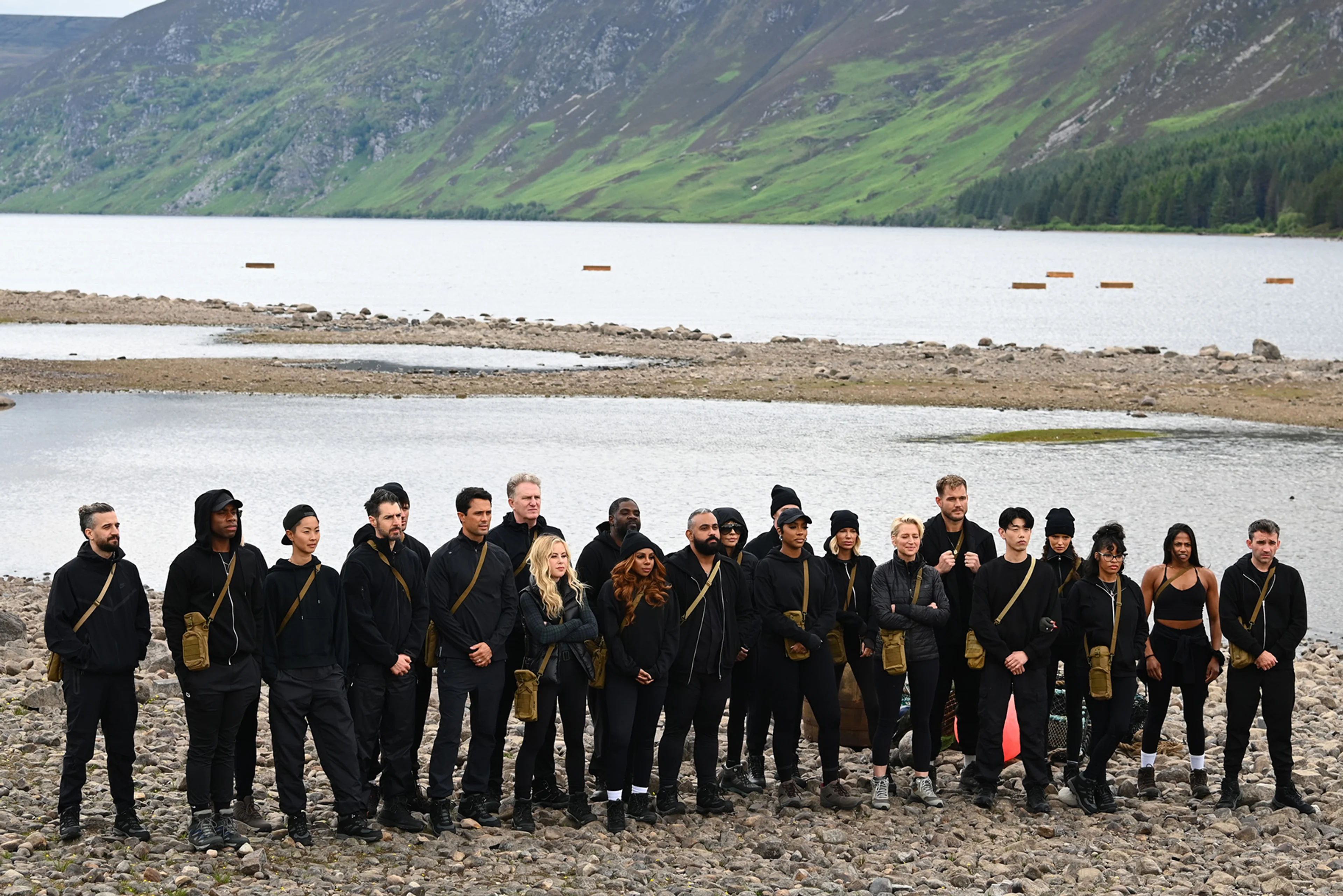 The Traitors Season 4 contestants stand beside a lake in the Scottish Highlands.