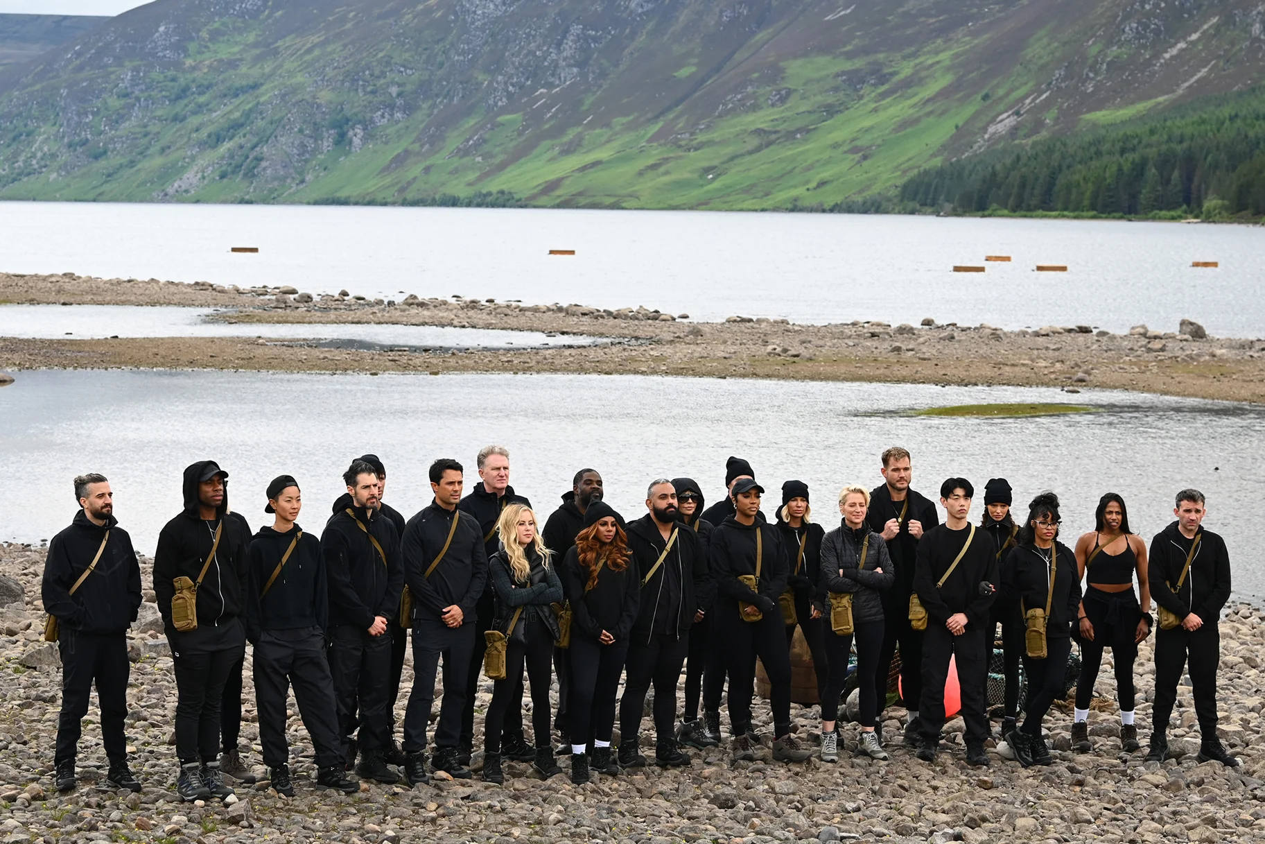 The Traitors Season 4 contestants stand beside a lake in the Scottish Highlands.