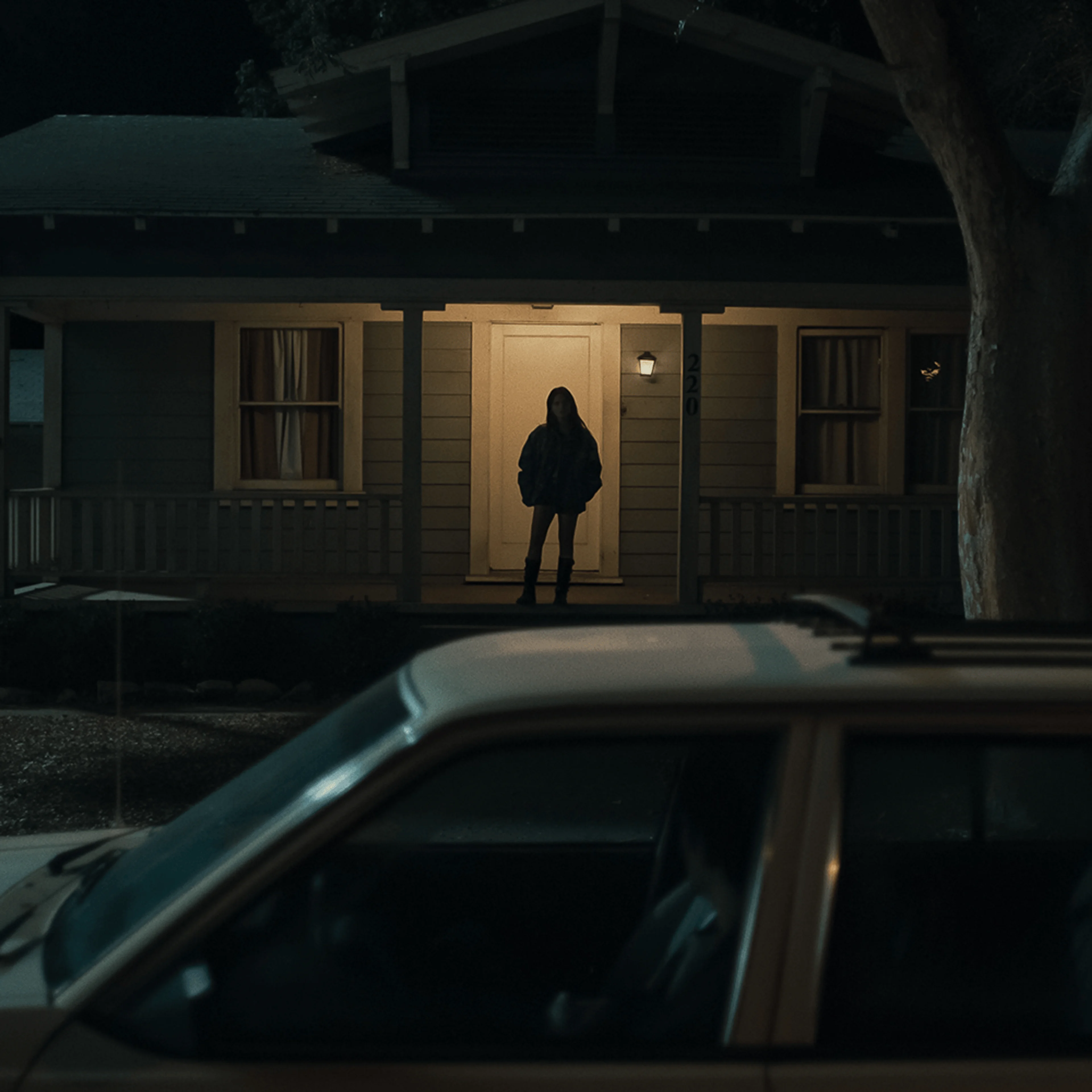 A woman stands outside a house at night in an official Obsession image.