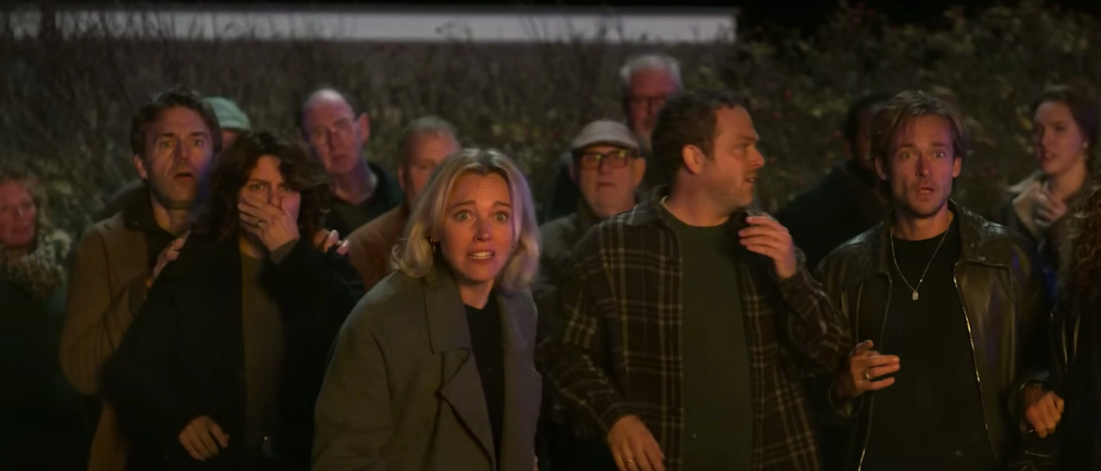 Dinner club members stare toward an unseen event outside at night in The Perfect Lie.
