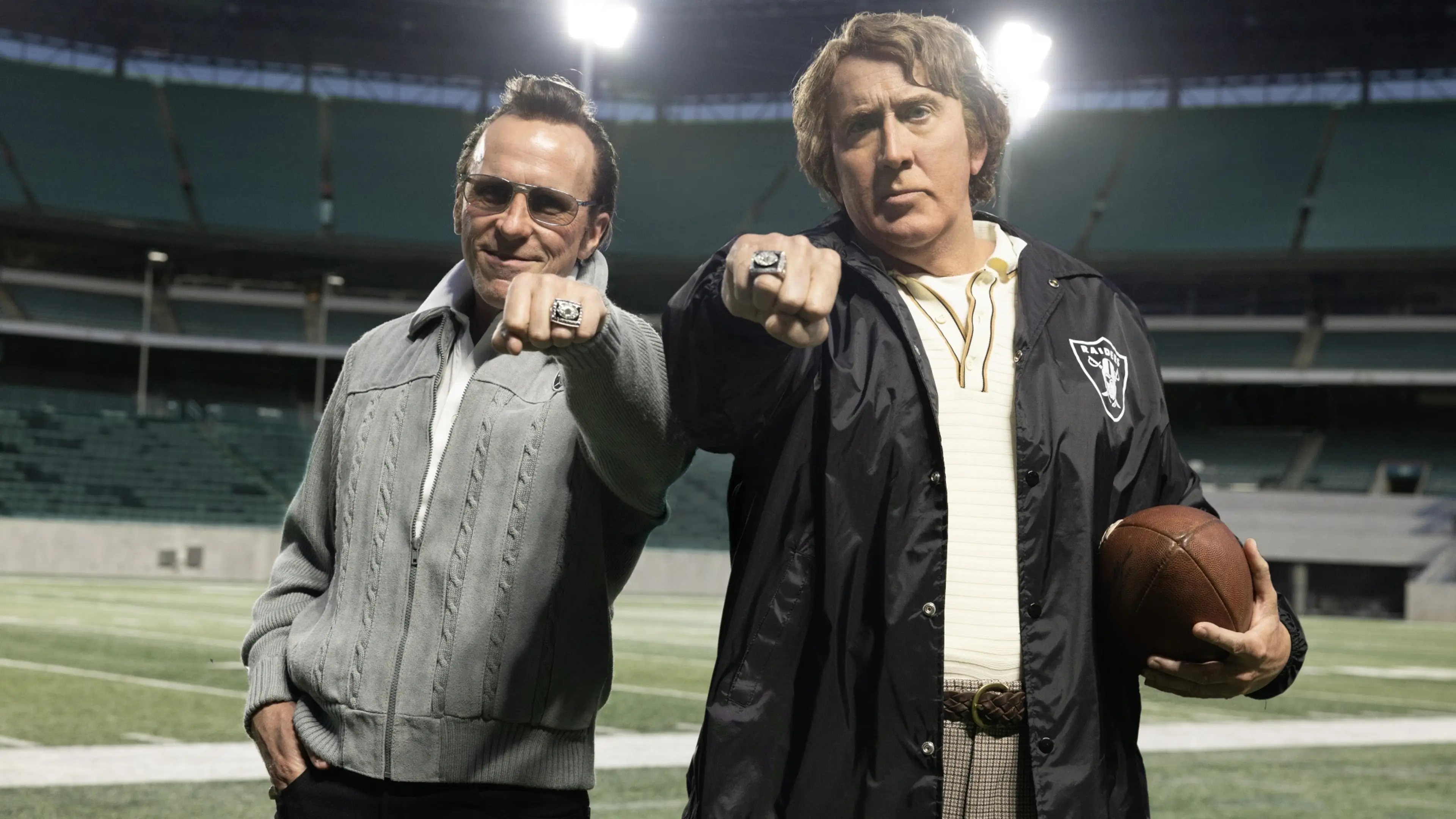 Christian Bale as Al Davis and Nicolas Cage as John Madden stand on a football field in Madden.