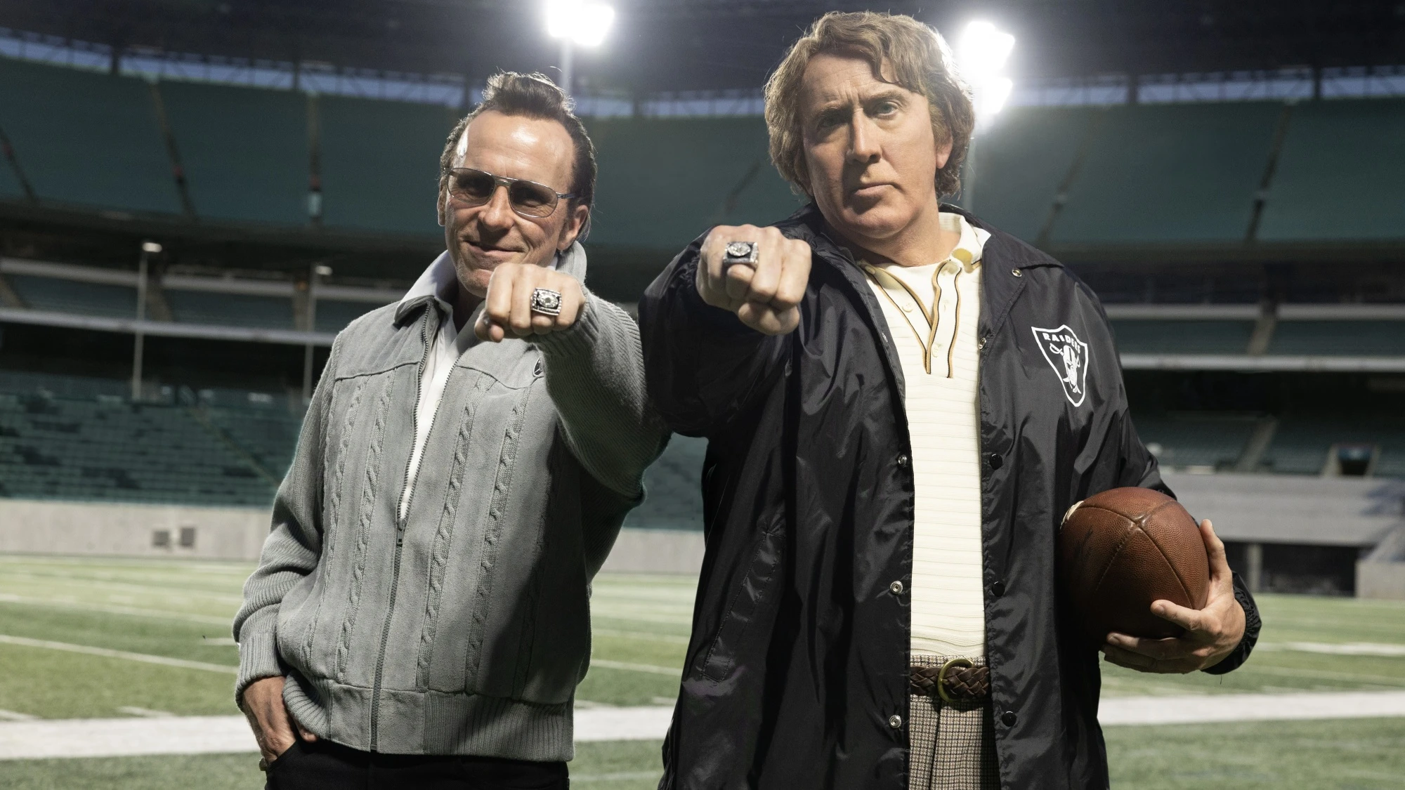 Christian Bale as Al Davis and Nicolas Cage as John Madden stand on a football field in Madden.