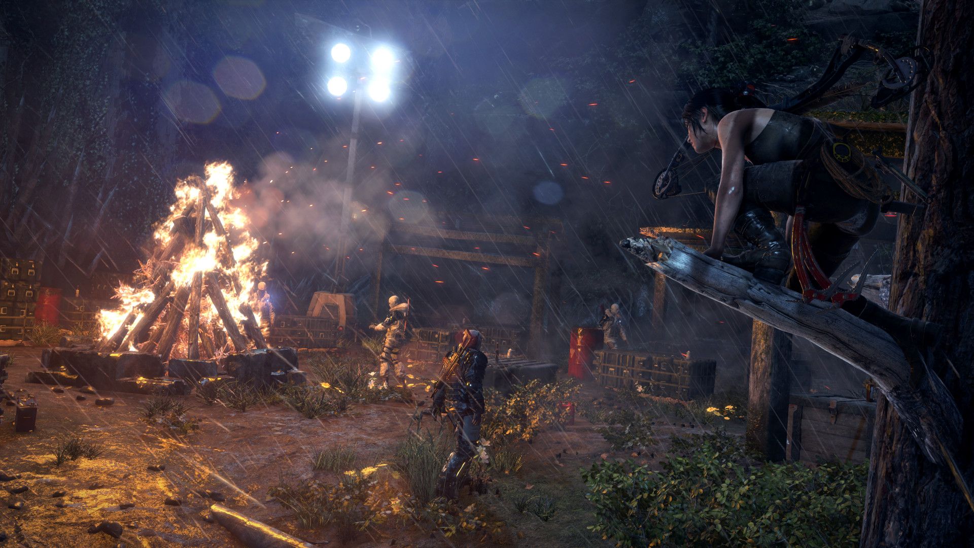 A firelit enemy camp appears in the distance from a dark rocky area.