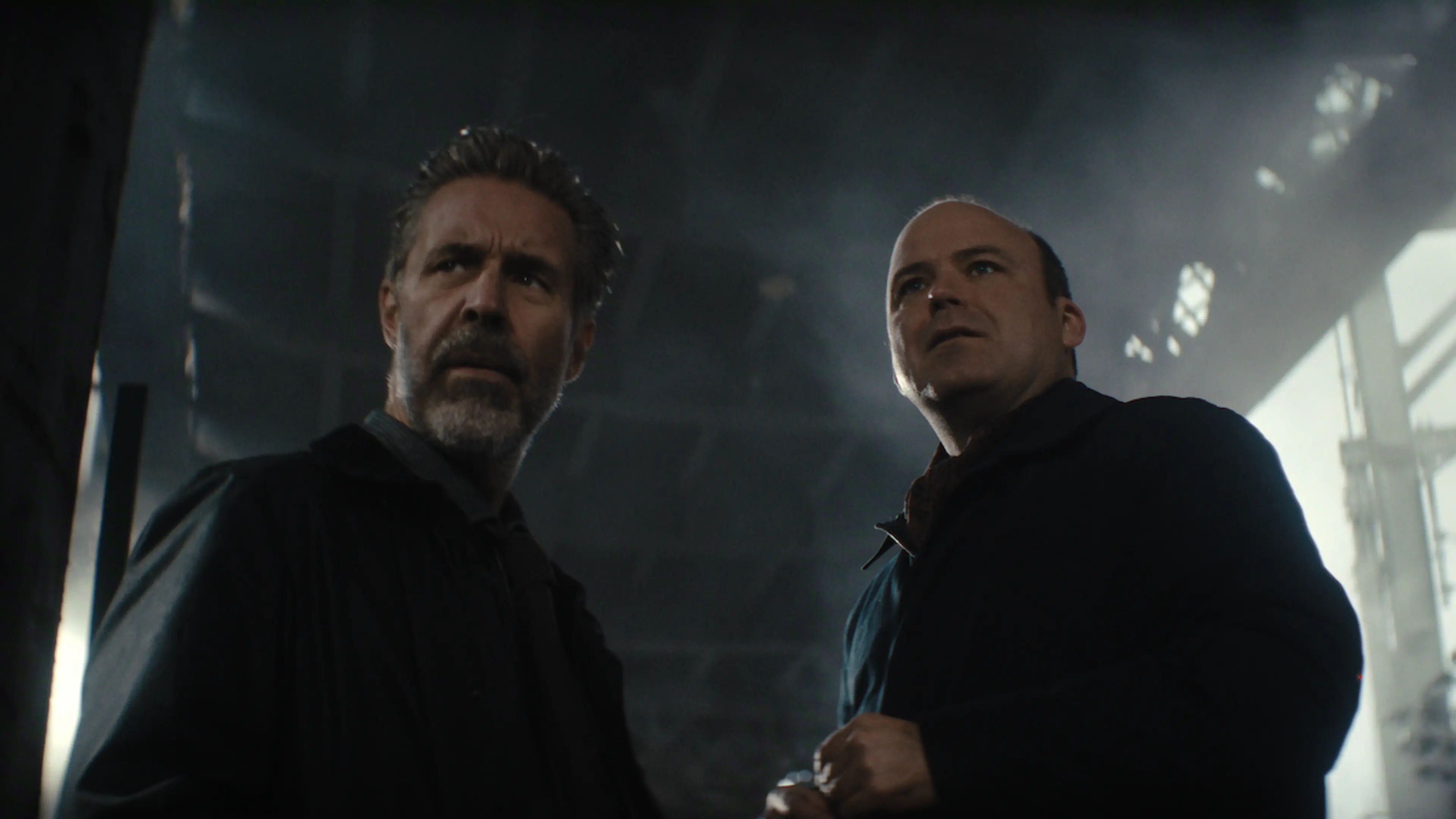 Two men stand in a dimly lit industrial room in a Blackmere first-look image.