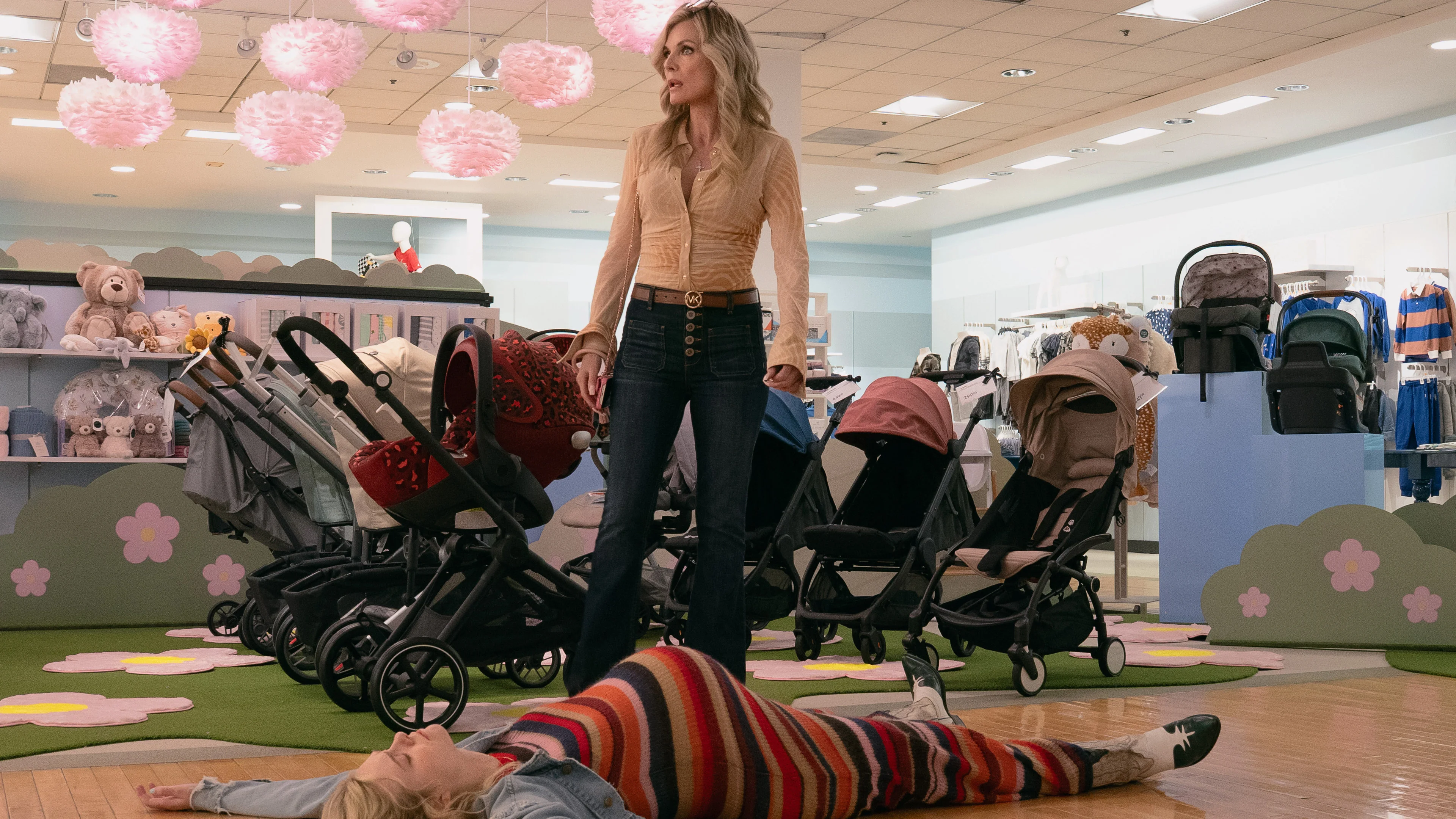 Pregnant Margo lies on the floor of a baby department while Shyanne stands beside her.